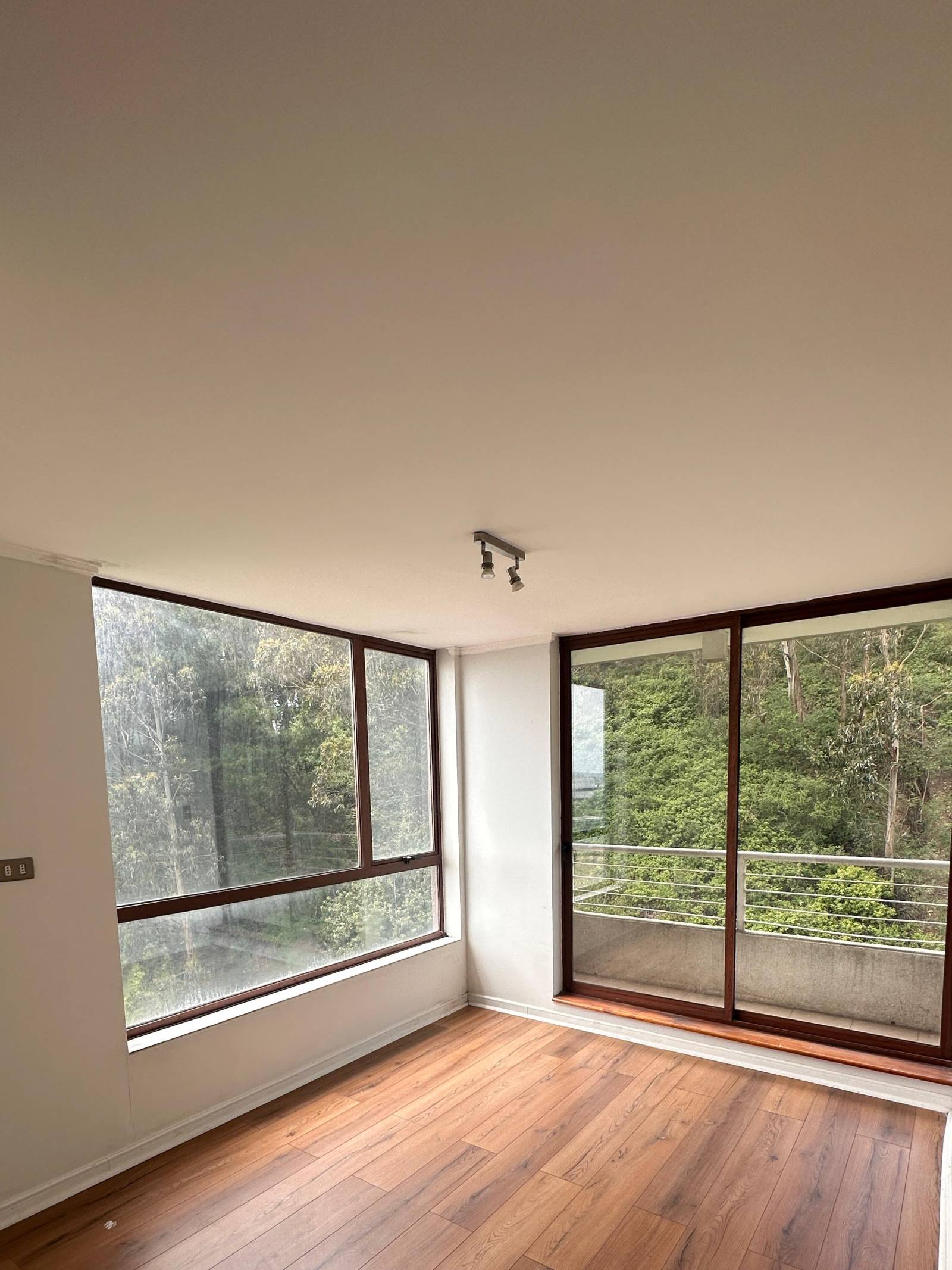 Dormitorio con piso laminado y ventanal hacia vegetación.