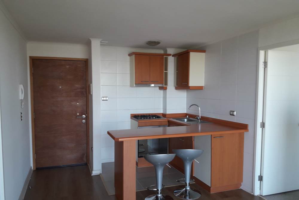 Cocina americana con muebles de madera, encimera y barra desayunadora.