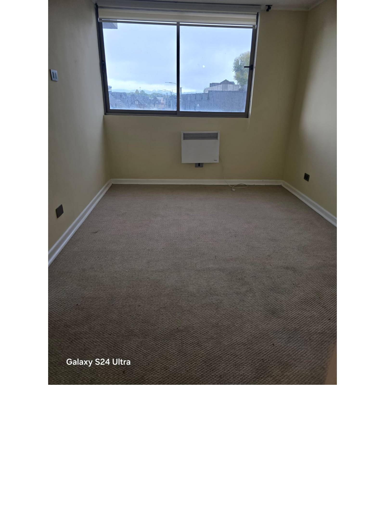 Dormitorio alfombrado con ventana y calefactor de pared.