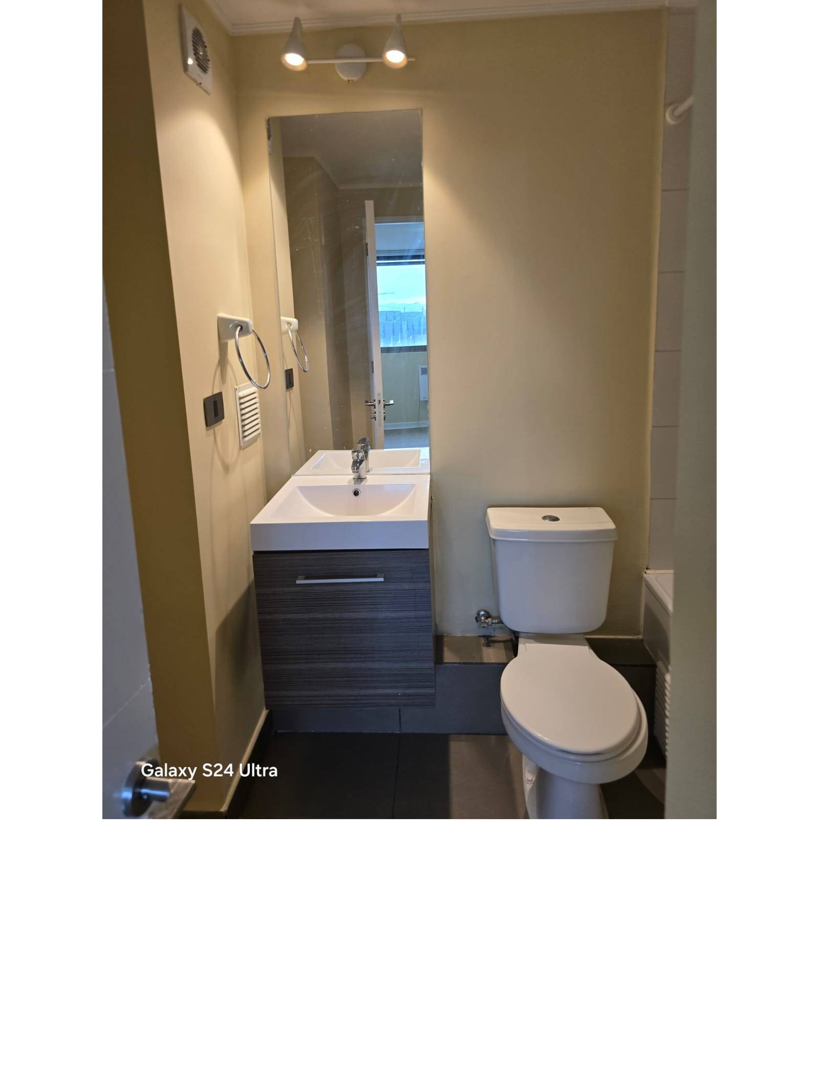 Baño con vanitorio moderno, espejo vertical y sanitario blanco.