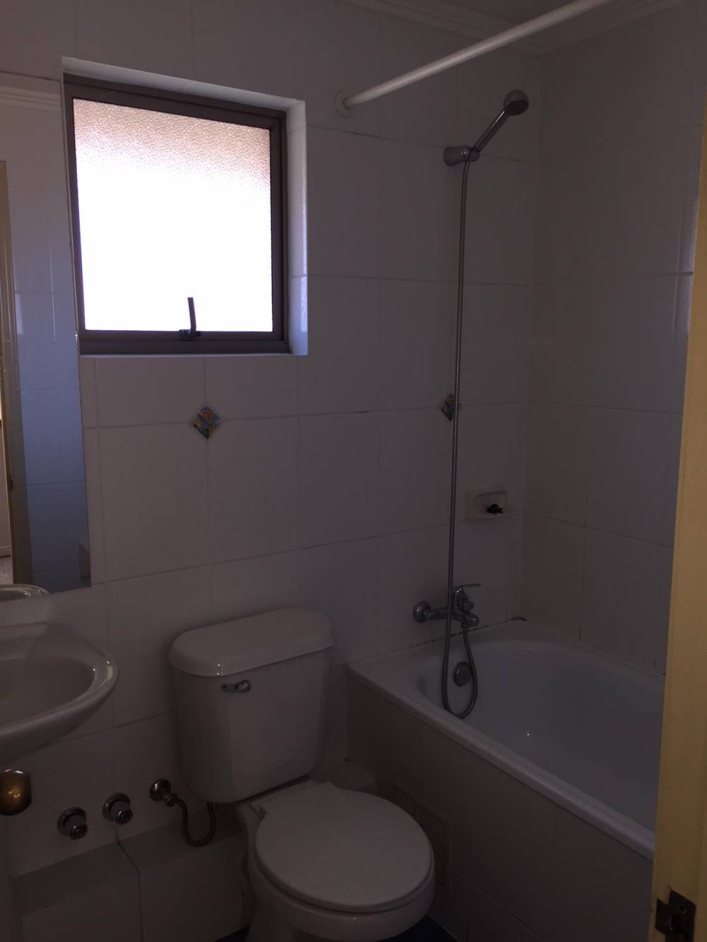 Baño principal con tina, inodoro y ventana pequeña.