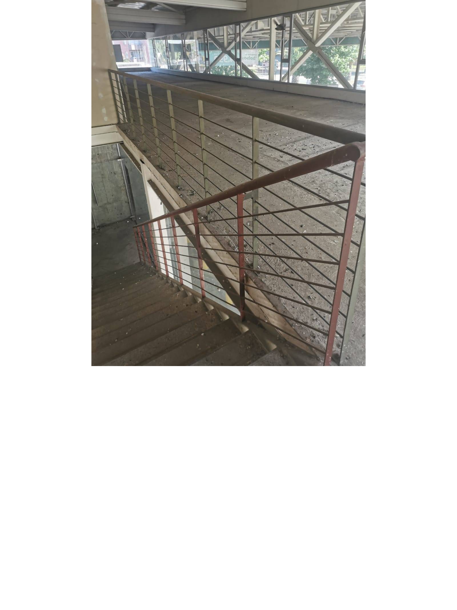 Vista descendente de escalera metálica con baranda en segundo nivel