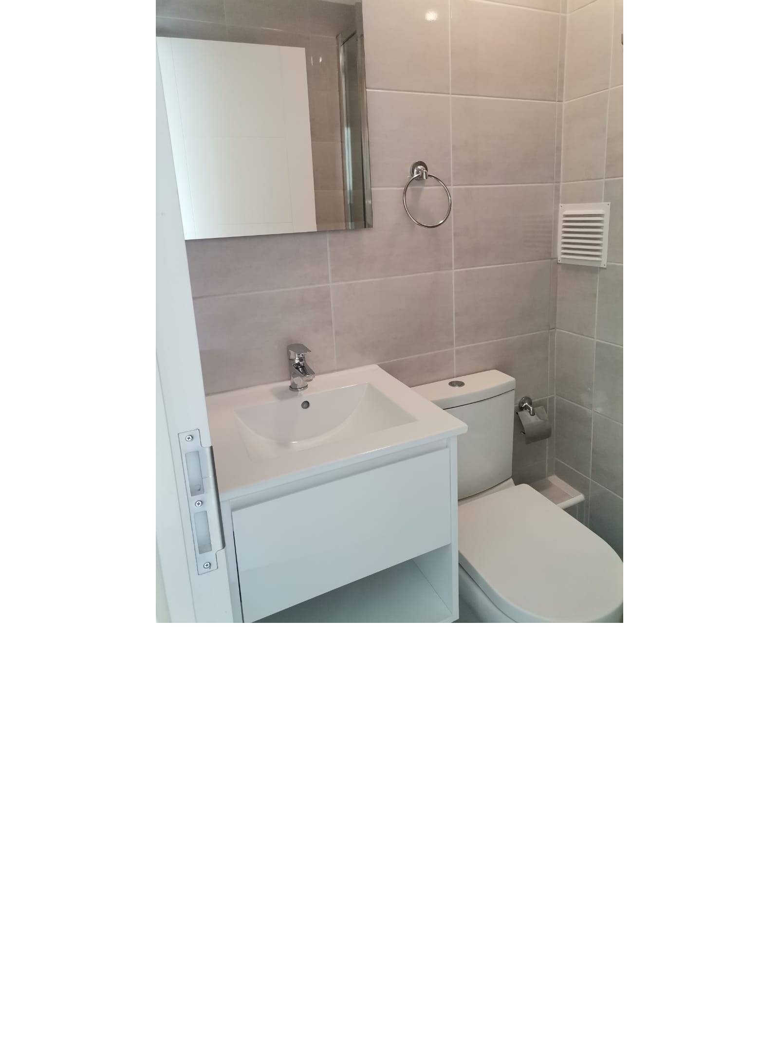 Vanitorio blanco con espejo mural e inodoro en baño.