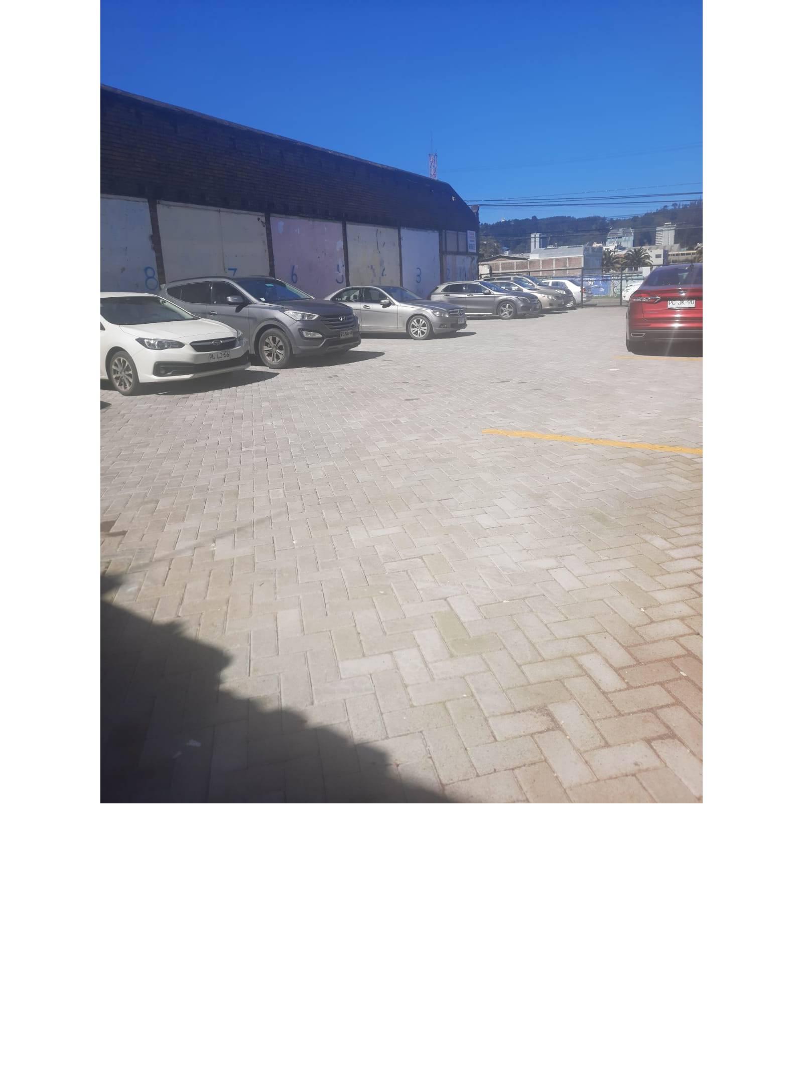 Canchón de estacionamiento adoquinado con filas de vehículos aparcados.