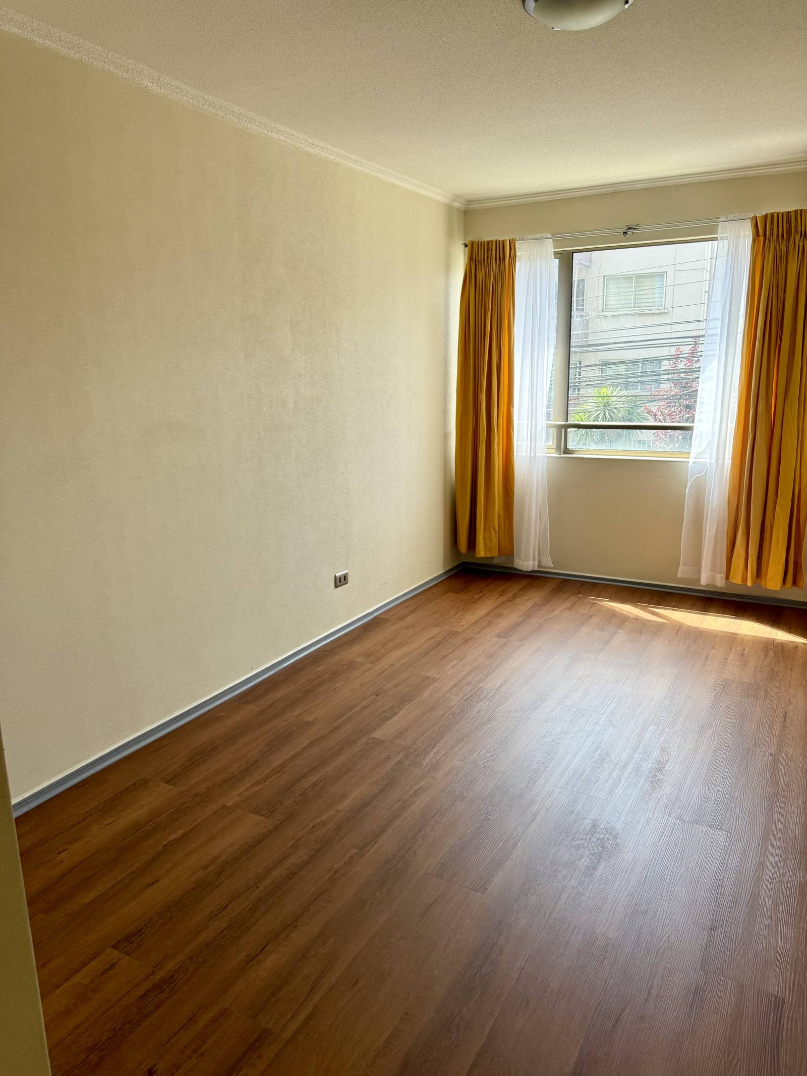 Dormitorio luminoso con cortinas amarillas y piso laminado.