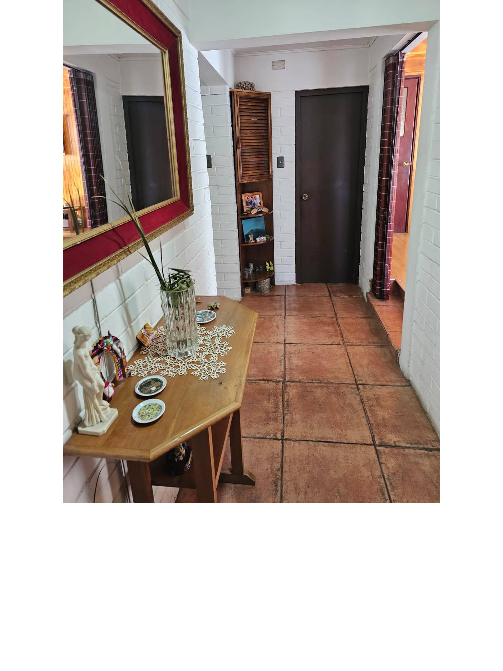 Hall de entrada con mesa lateral de madera y piso cerámico.
