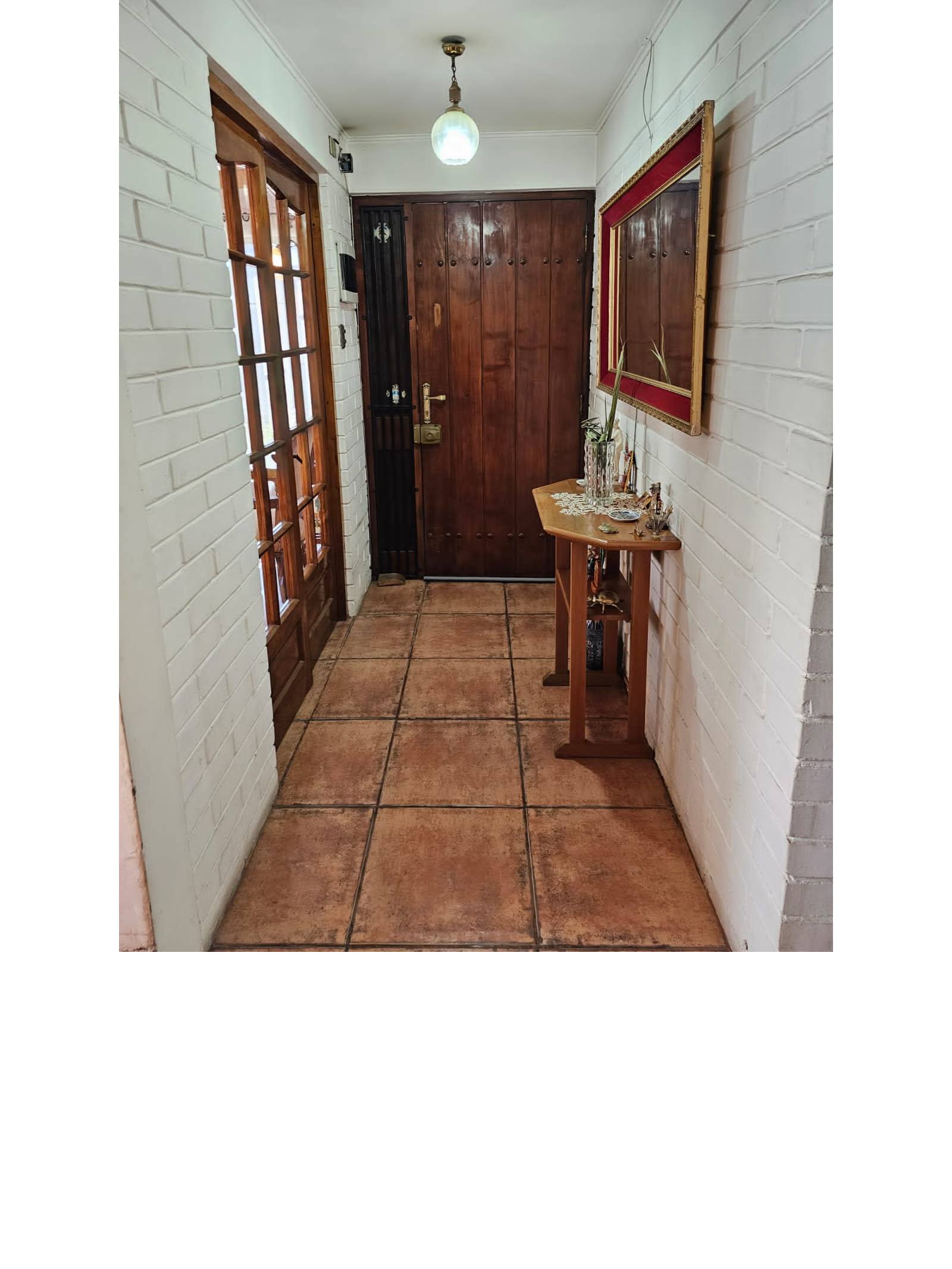 Pasillo hacia puerta principal de madera con piso cerámico rústico.