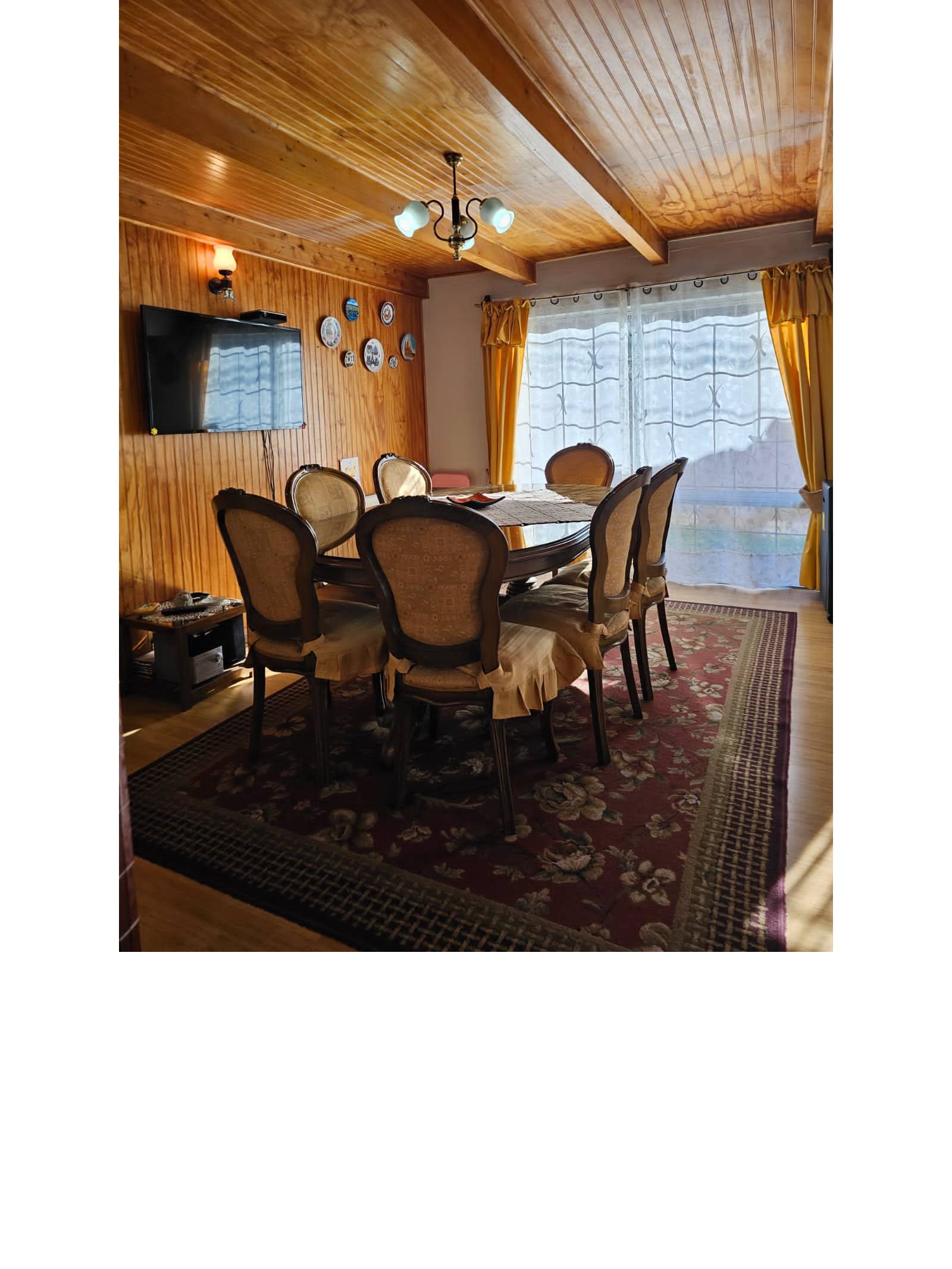 Comedor con mesa redonda, sillas clásicas y cielo de madera.