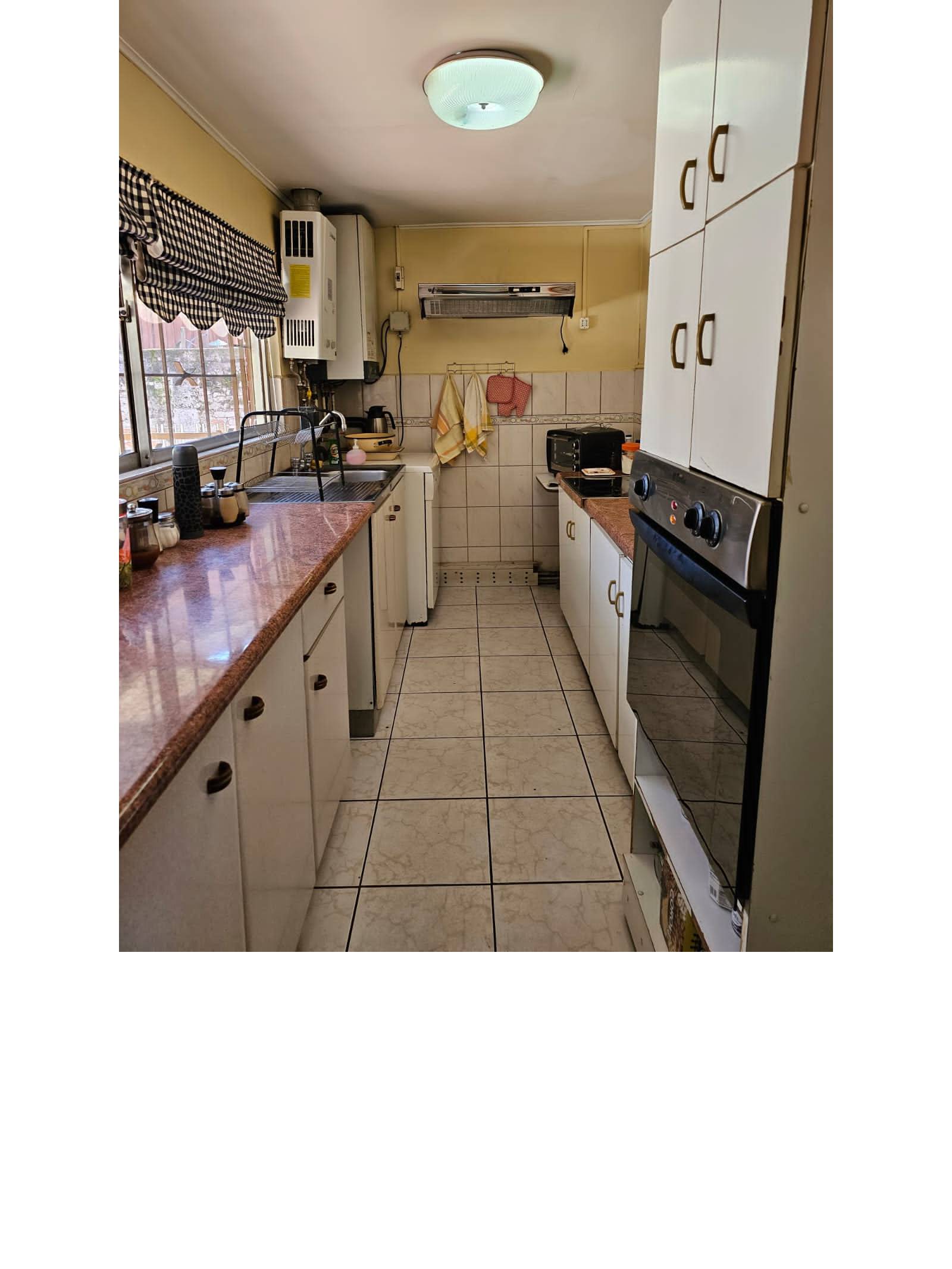 Cocina alargada amoblada con horno empotrado y mesón de granito.