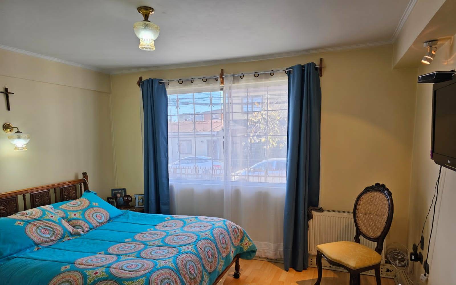 Dormitorio principal con cama matrimonial y ventanal con cortinas azules.