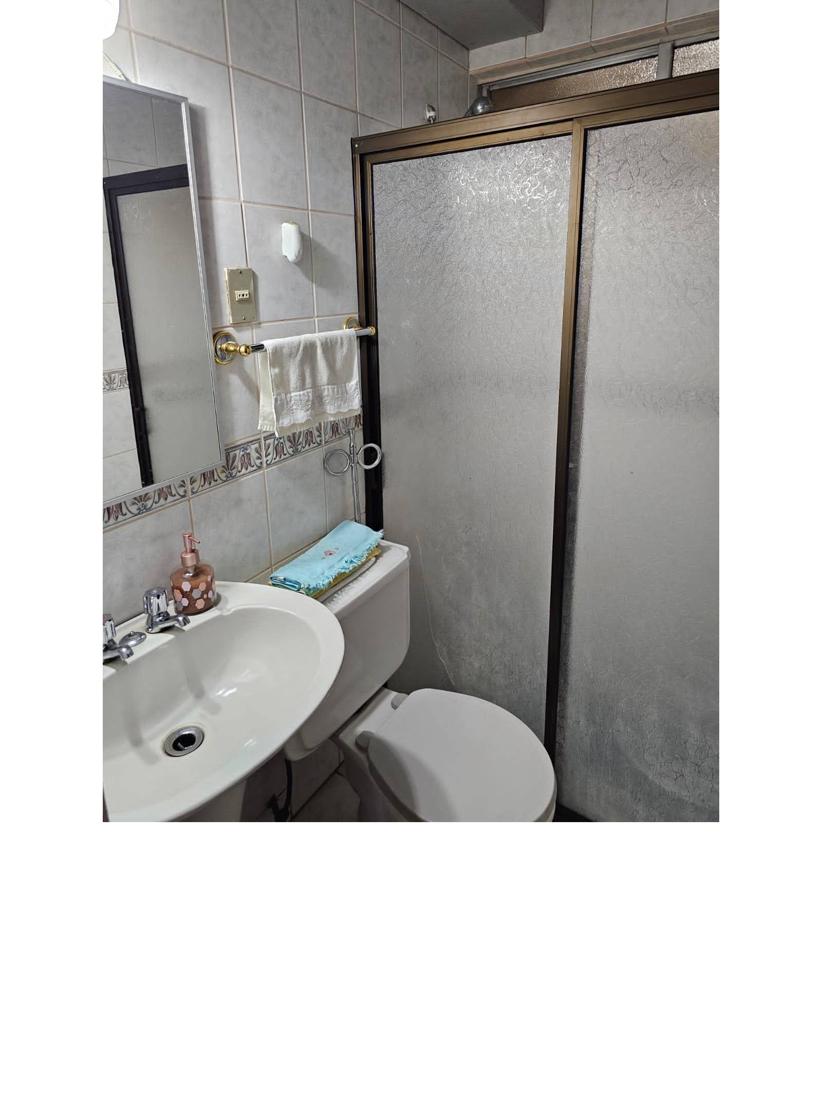 Segundo baño con lavamanos, inodoro y mampara de ducha.