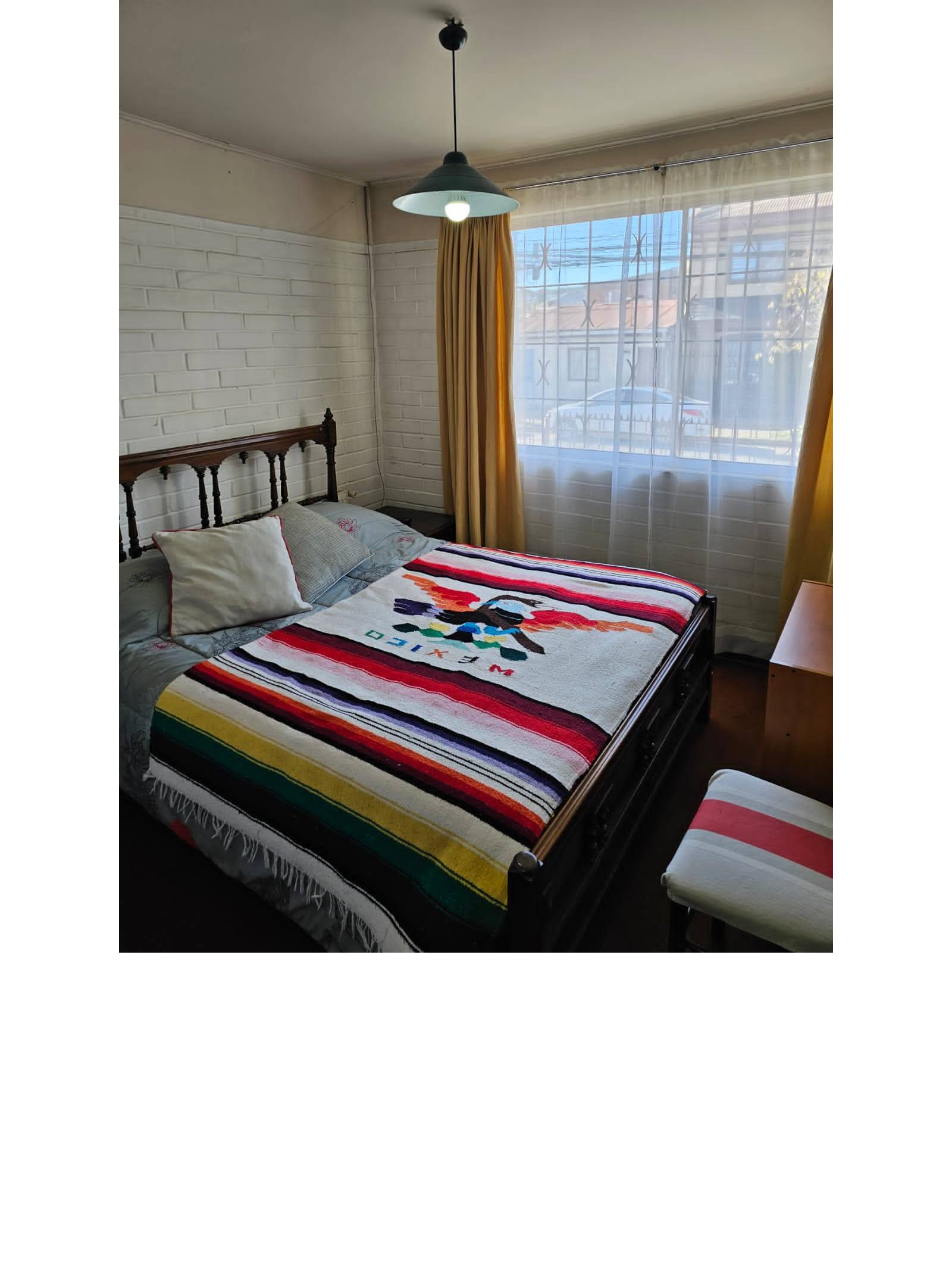 Dormitorio con cama de madera y ventana amplia hacia el exterior.