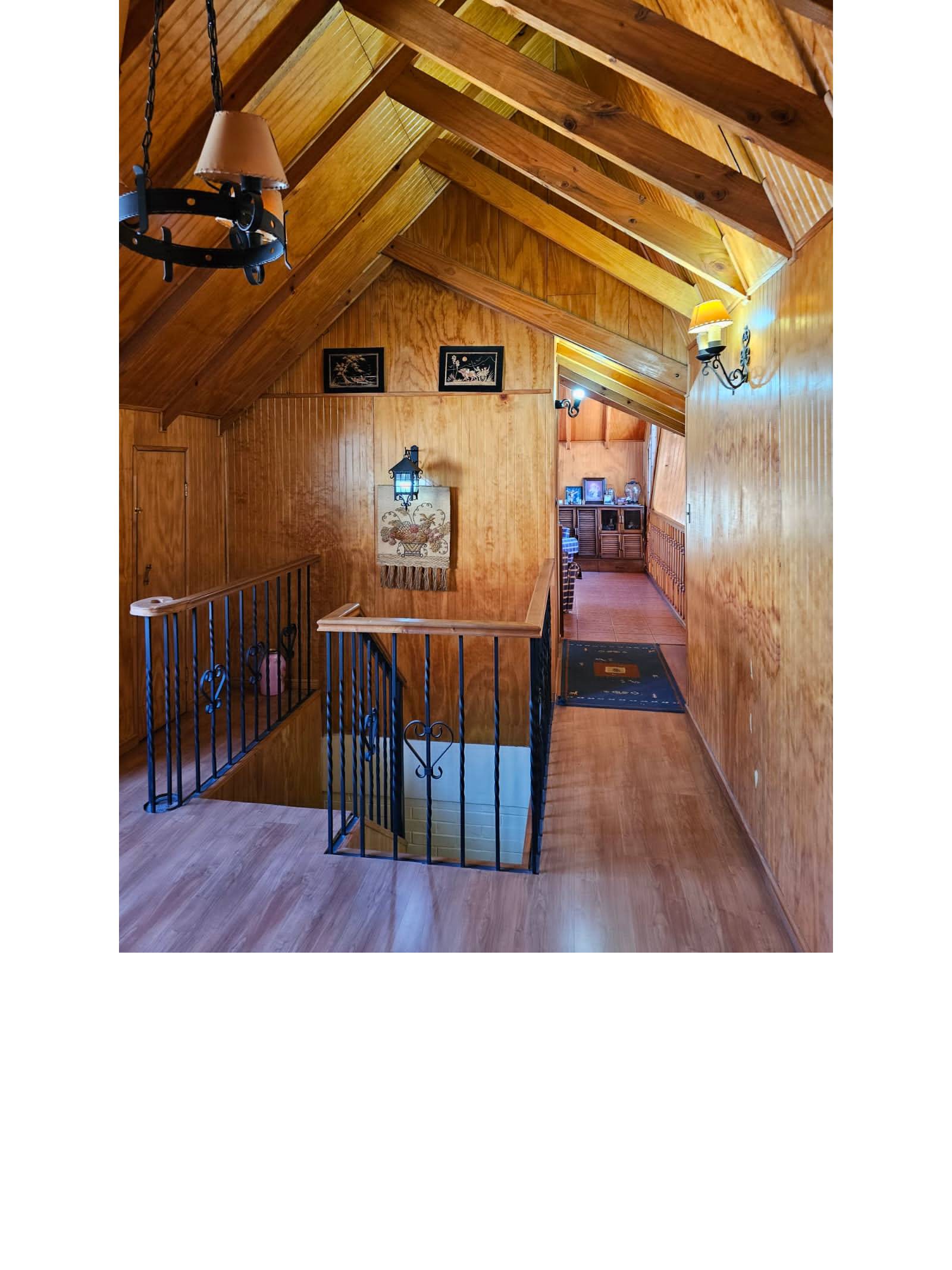Escalera y pasillo superior con techos altos y revestimiento de madera.