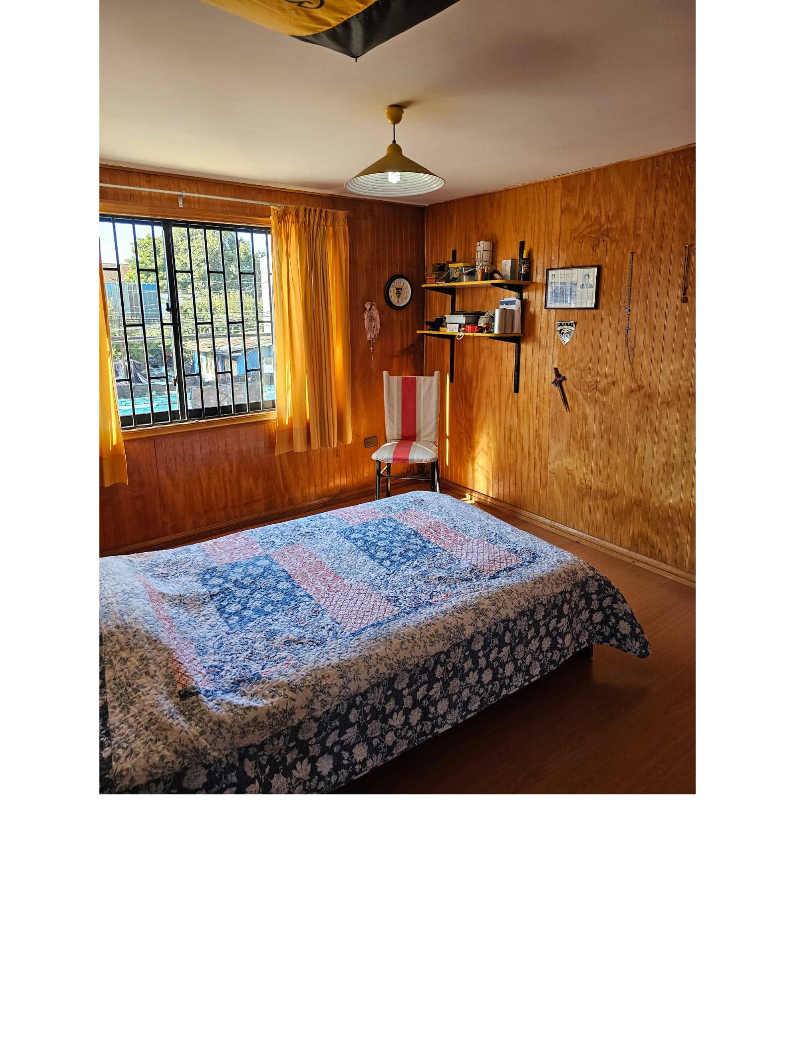 Dormitorio con paredes de madera, cama y ventana lateral soleada.