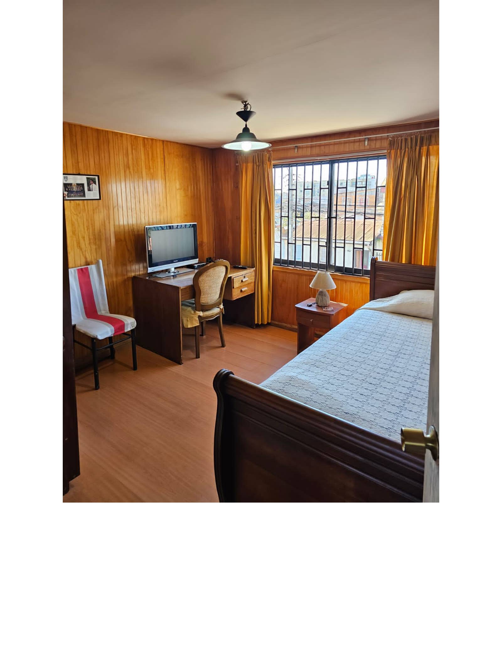 Dormitorio con cama individual, escritorio y paredes revestidas en madera.