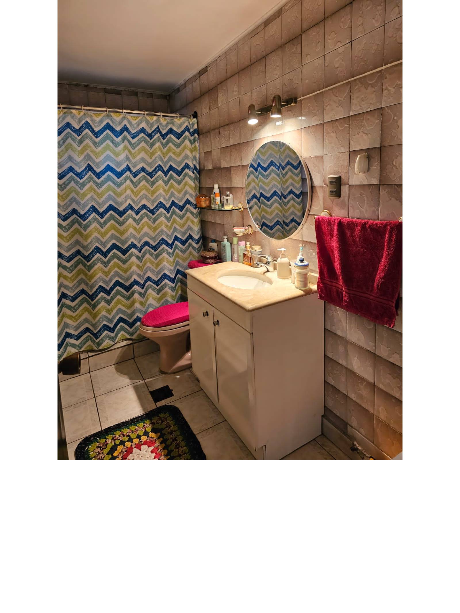 Baño con vanitorio blanco, espejo redondo y cortina estampada.