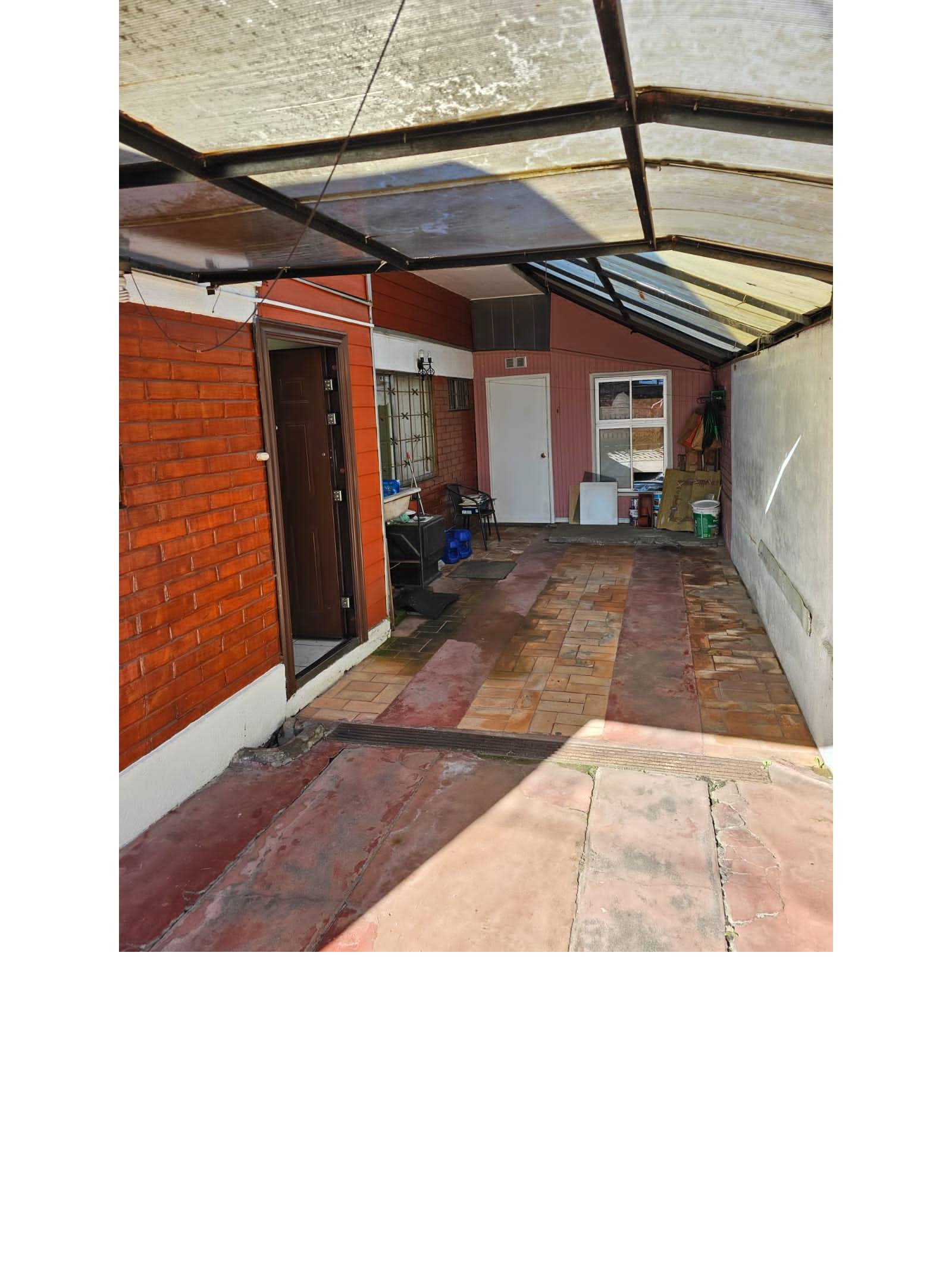 Patio lateral techado con piso de baldosas y paredes de ladrillo.