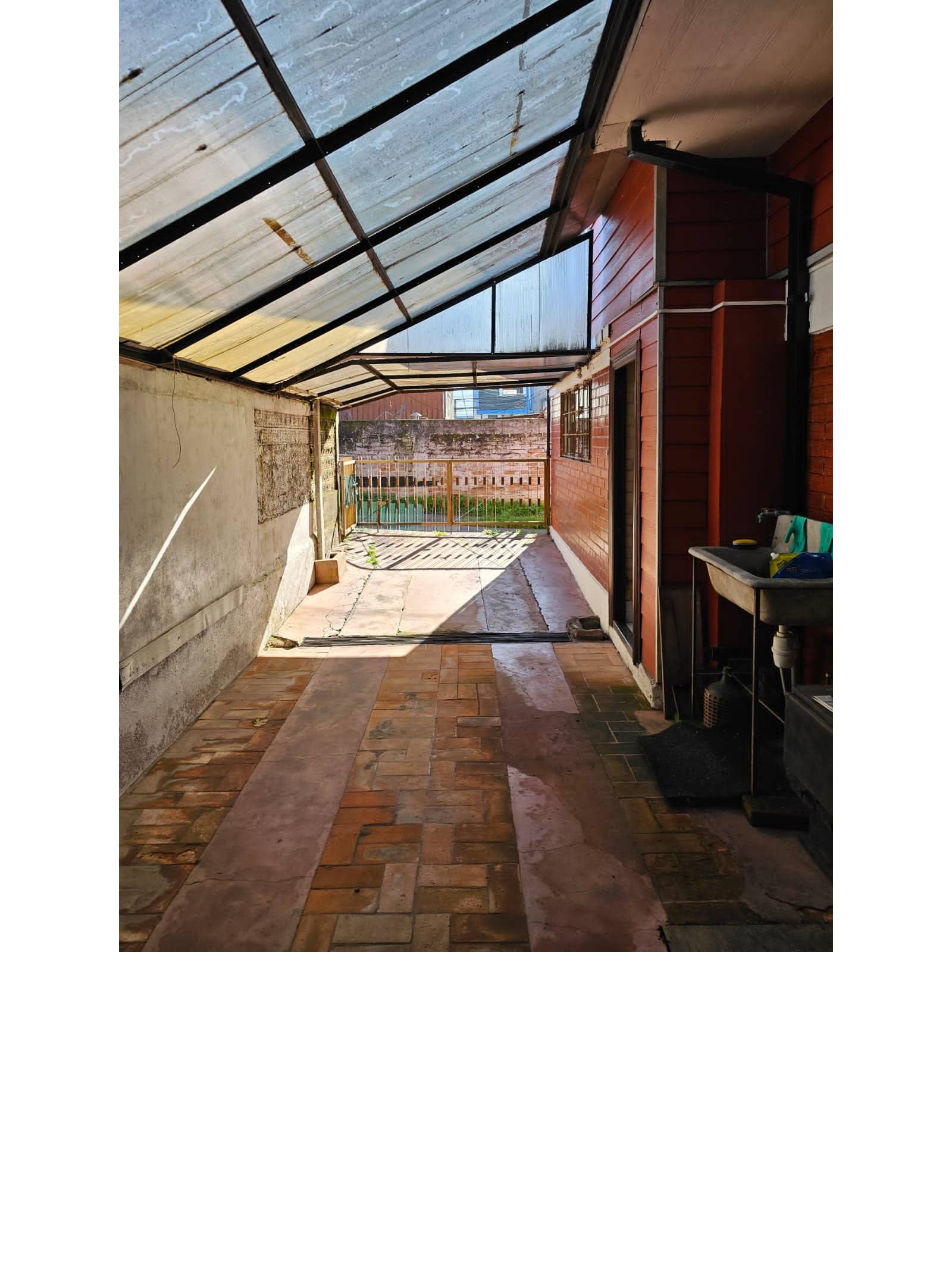 Patio techado tipo galería con lavadero y acceso a portón.