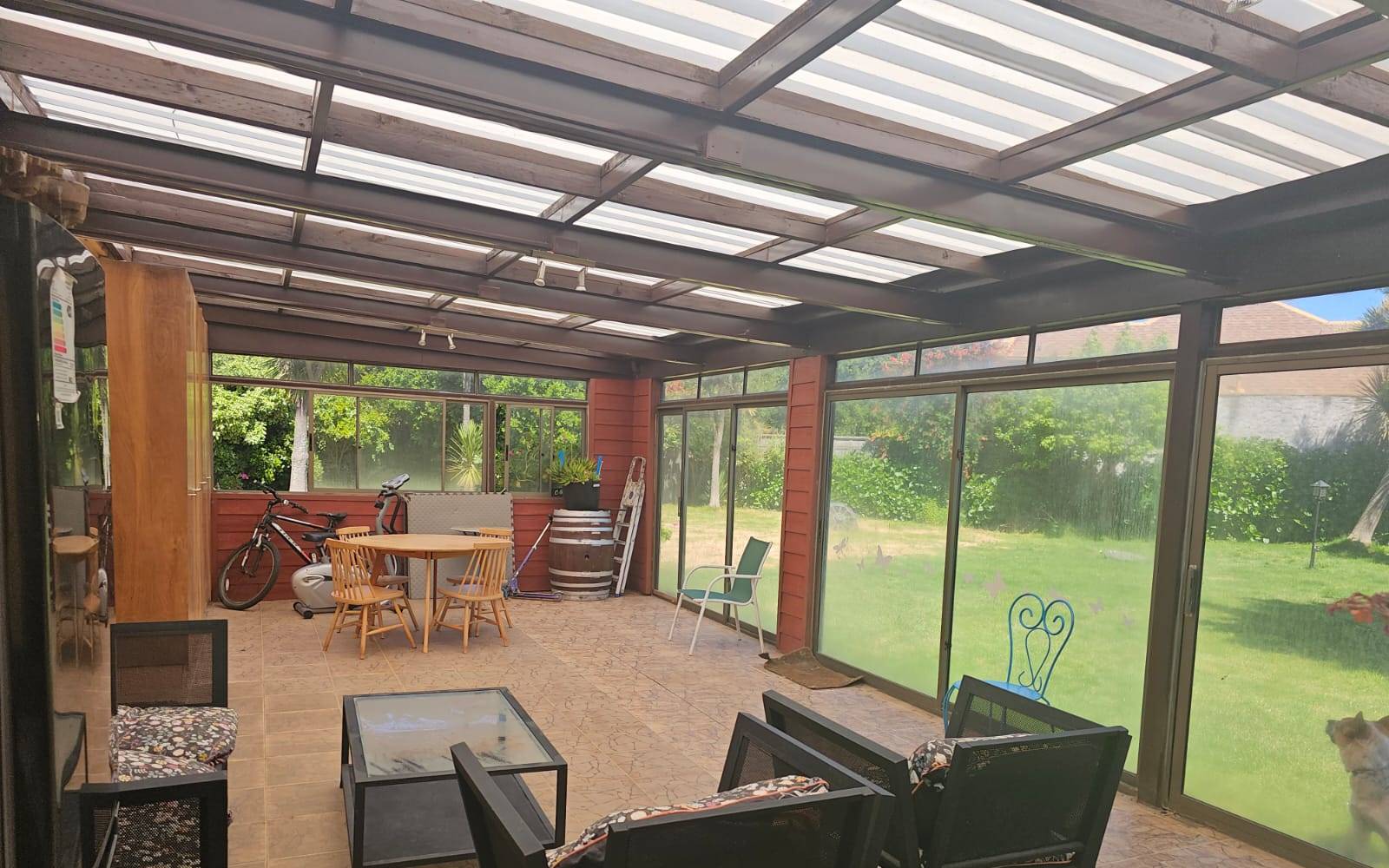 Terraza techada con cerramientos de vidrio y vista al jardín.