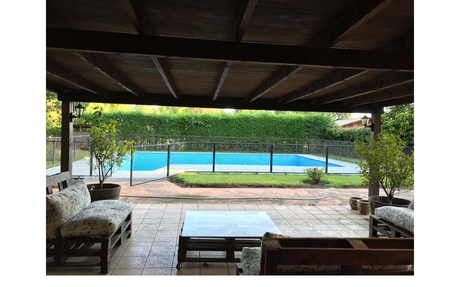 Terraza techada con living rústico frente a piscina con reja.