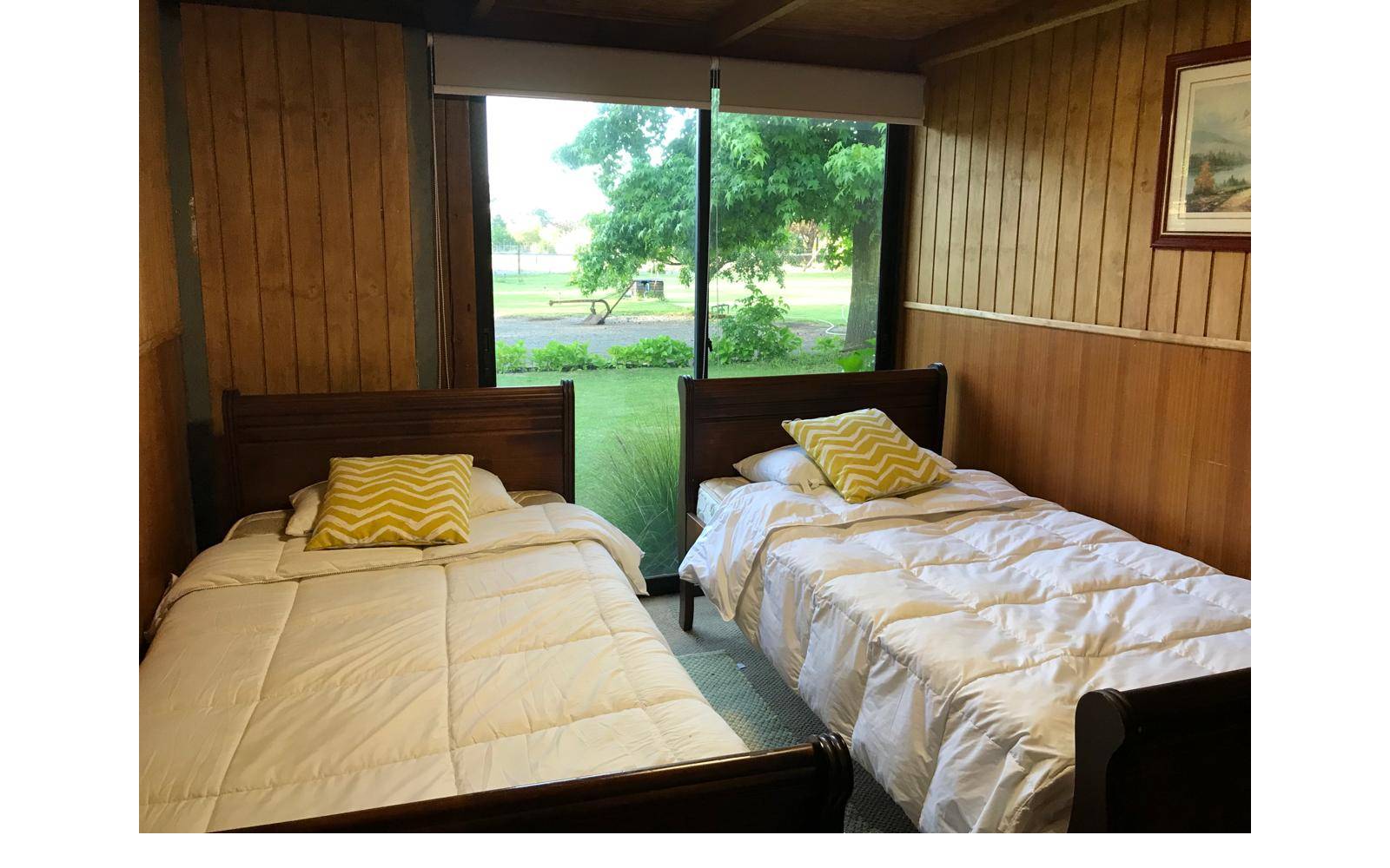 Dormitorio con dos camas individuales y ventanal a prado verde.