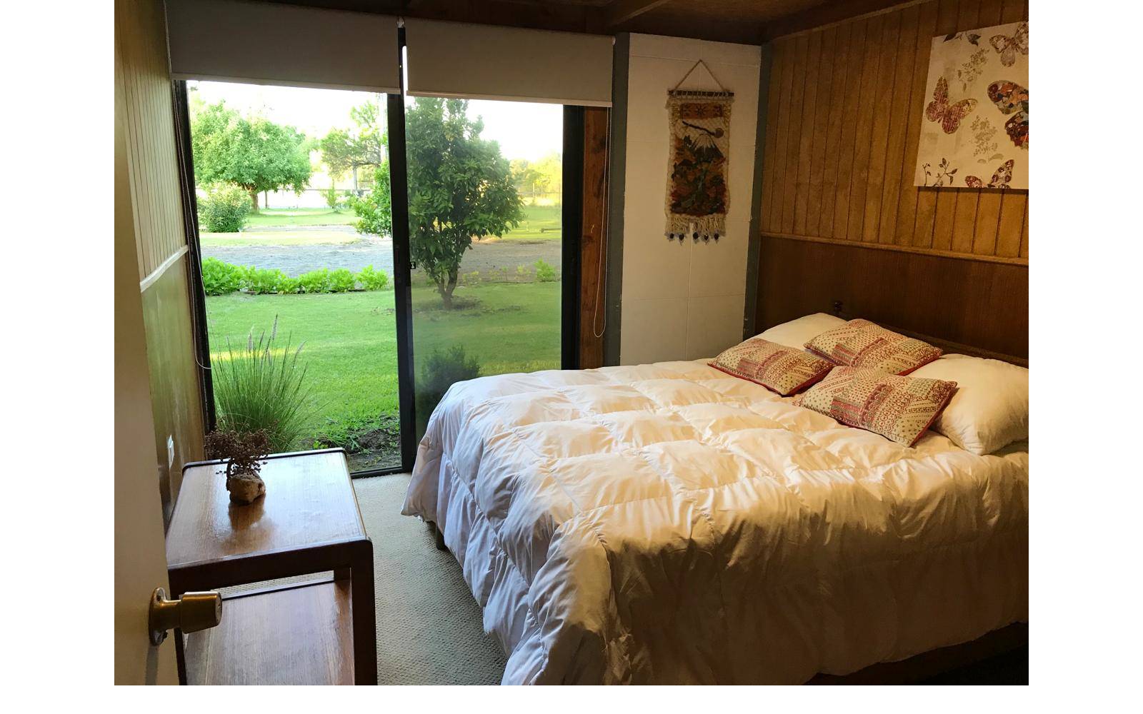 Dormitorio con cama matrimonial, paredes de madera y ventanal.