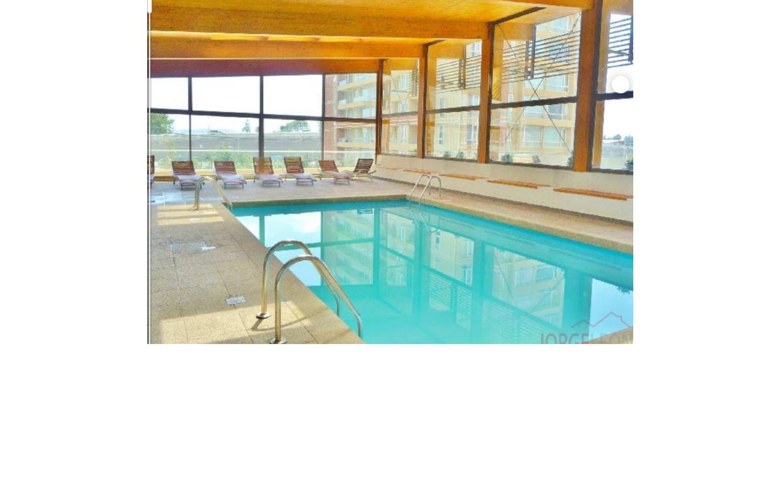 Piscina techada y climatizada del edificio con reposeras al fondo.