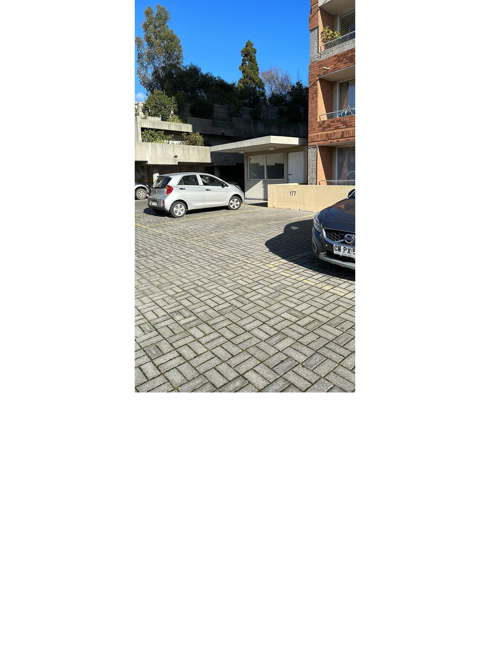 Estacionamiento exterior pavimentado con autos frente al edificio.