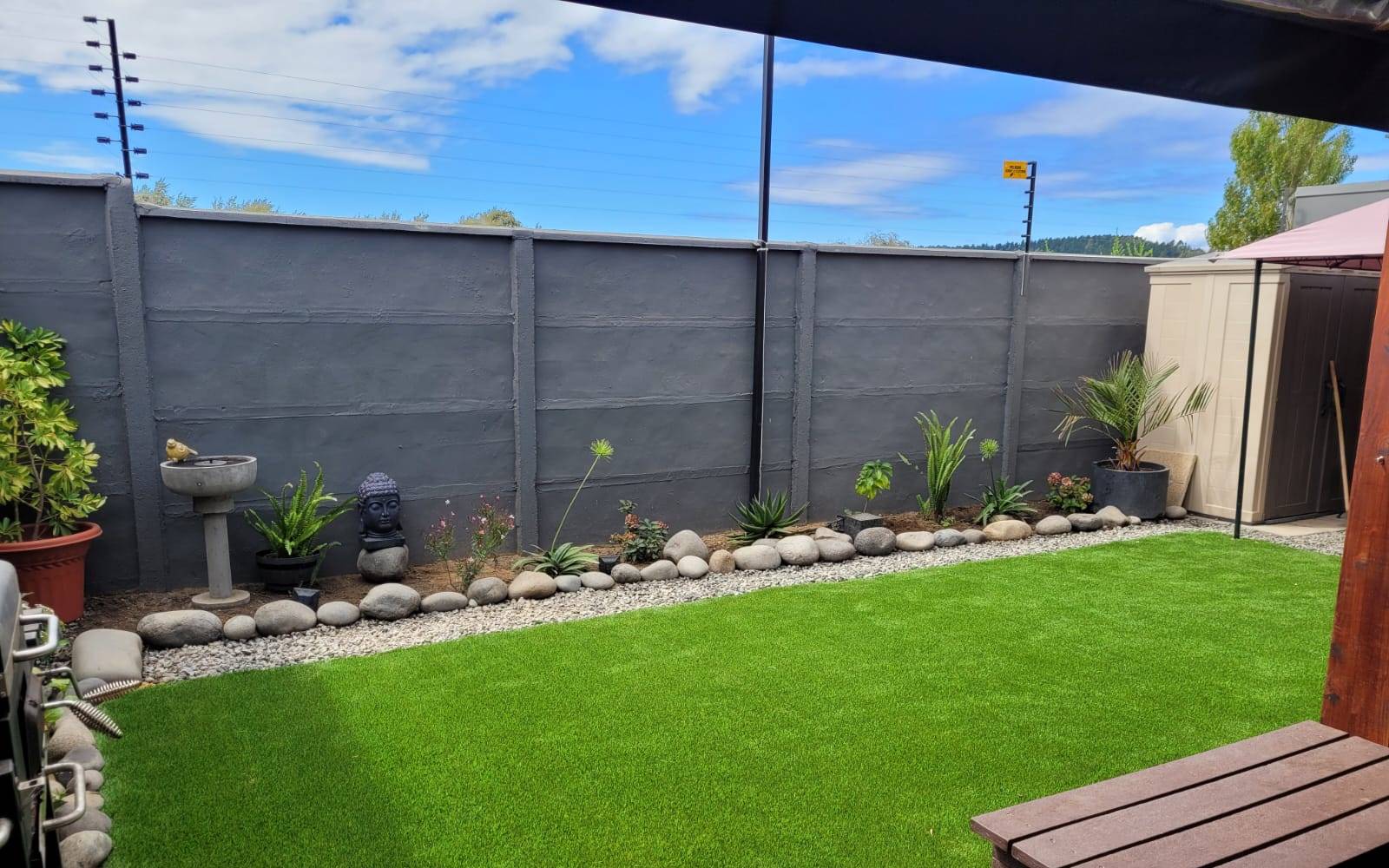 Patio con césped sintético y cantero de piedras perimetral