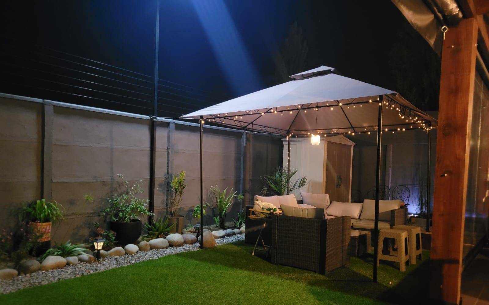 Pérgola iluminada con living exterior en patio nocturno
