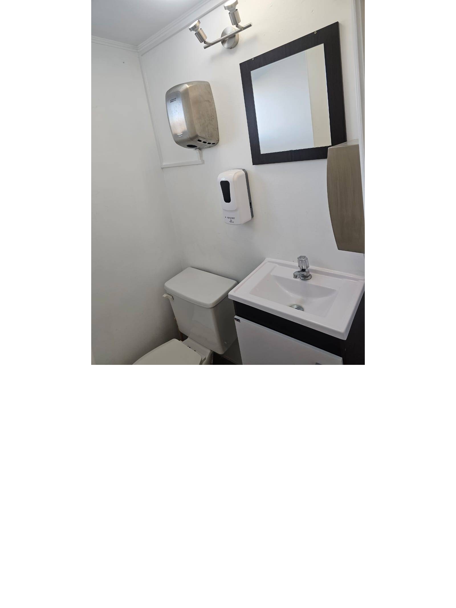 Baño con lavamanos, inodoro, espejo y dispensadores