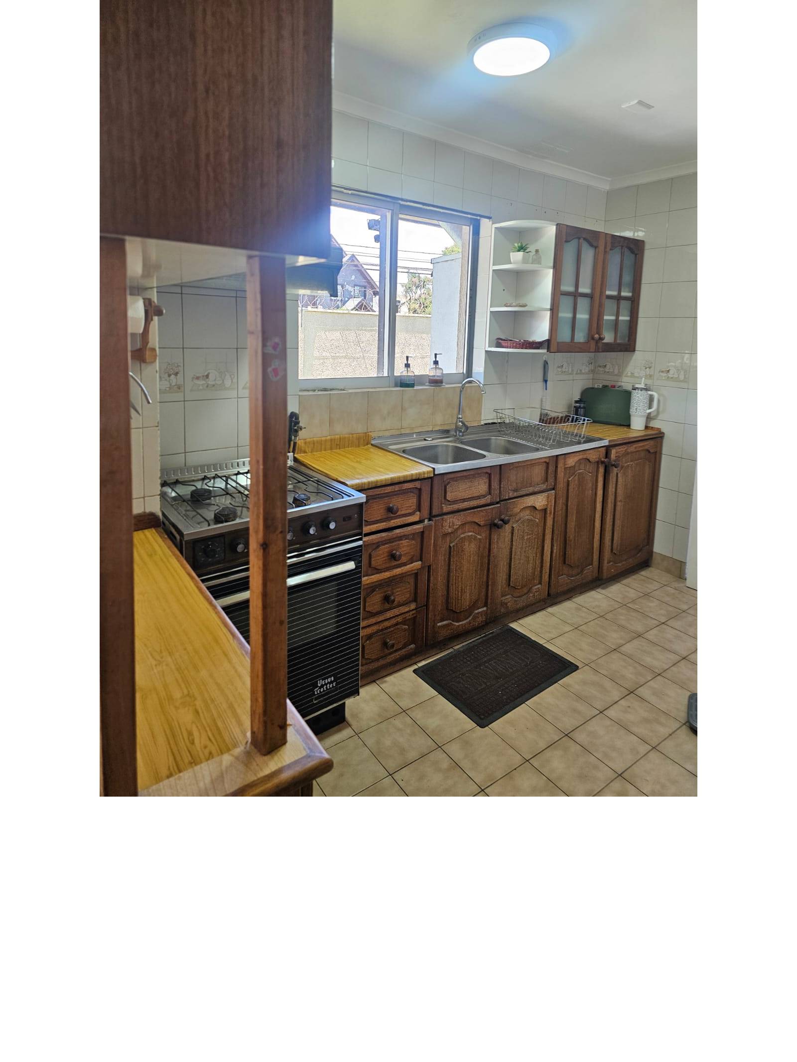 Cocina tradicional con muebles de madera y lavaplatos bajo ventana