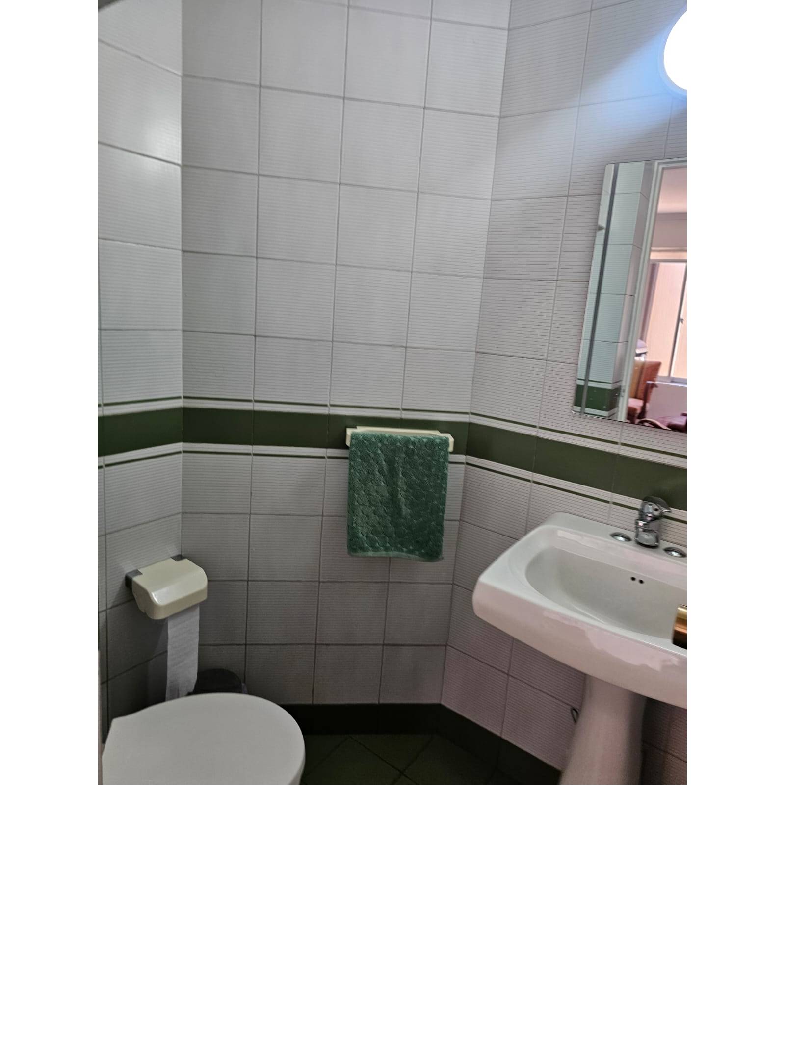 Baño con paredes cerámicas, lavamanos de pedestal e inodoro