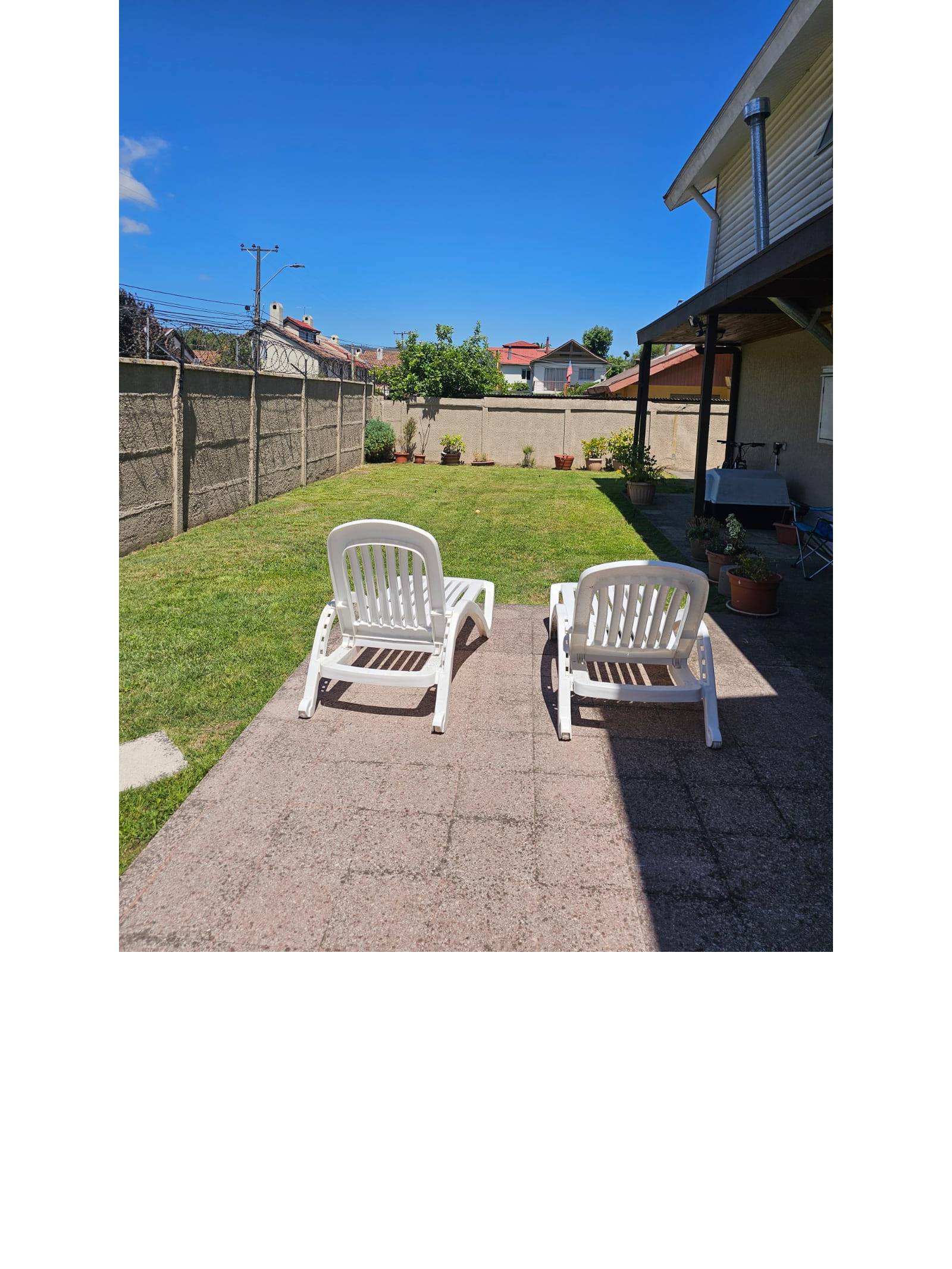 Patio soleado con césped verde, pandereta perimetral y reposeras
