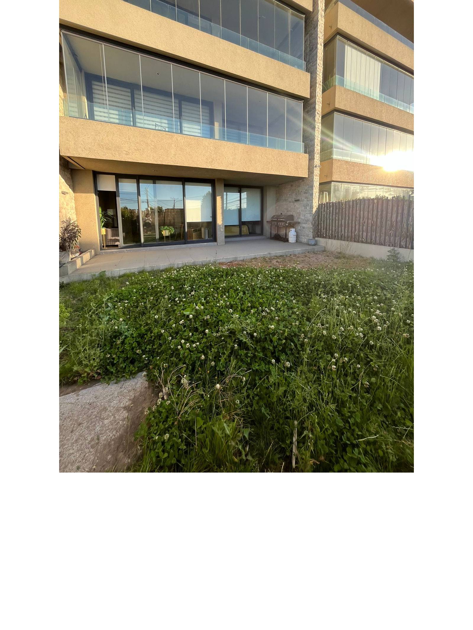 Patio exterior con césped y vista hacia terraza del departamento