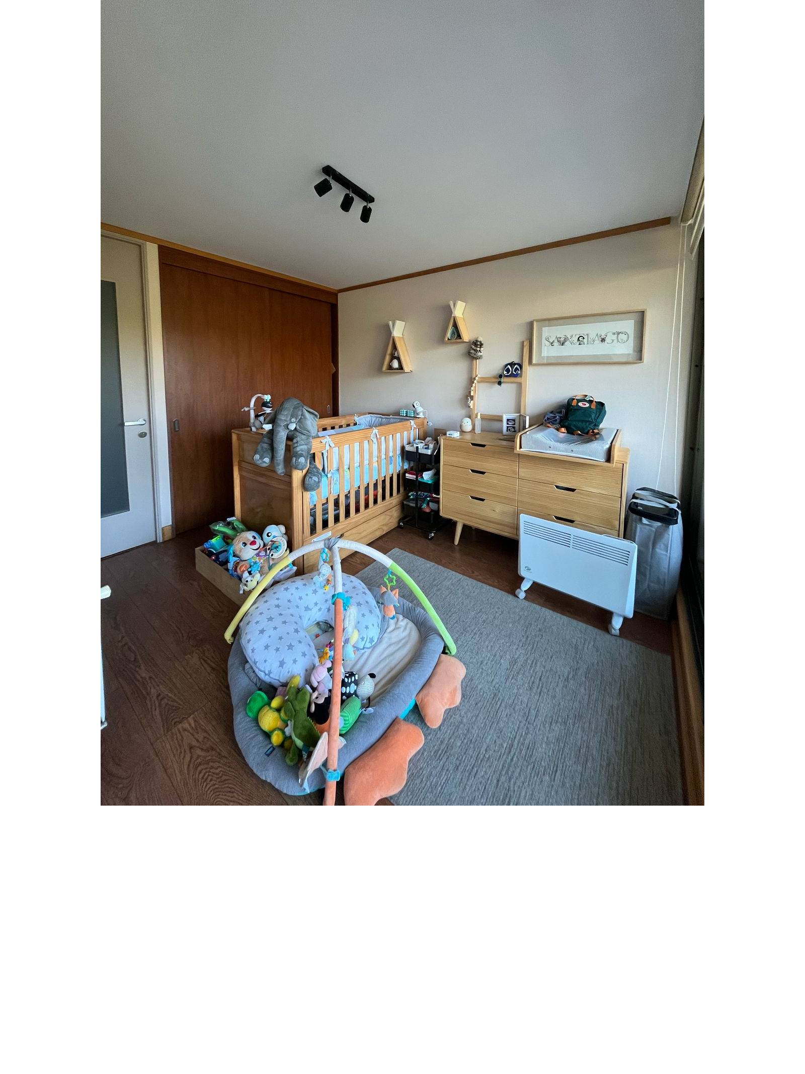 Dormitorio infantil con cuna de madera, cajonera y alfombra.