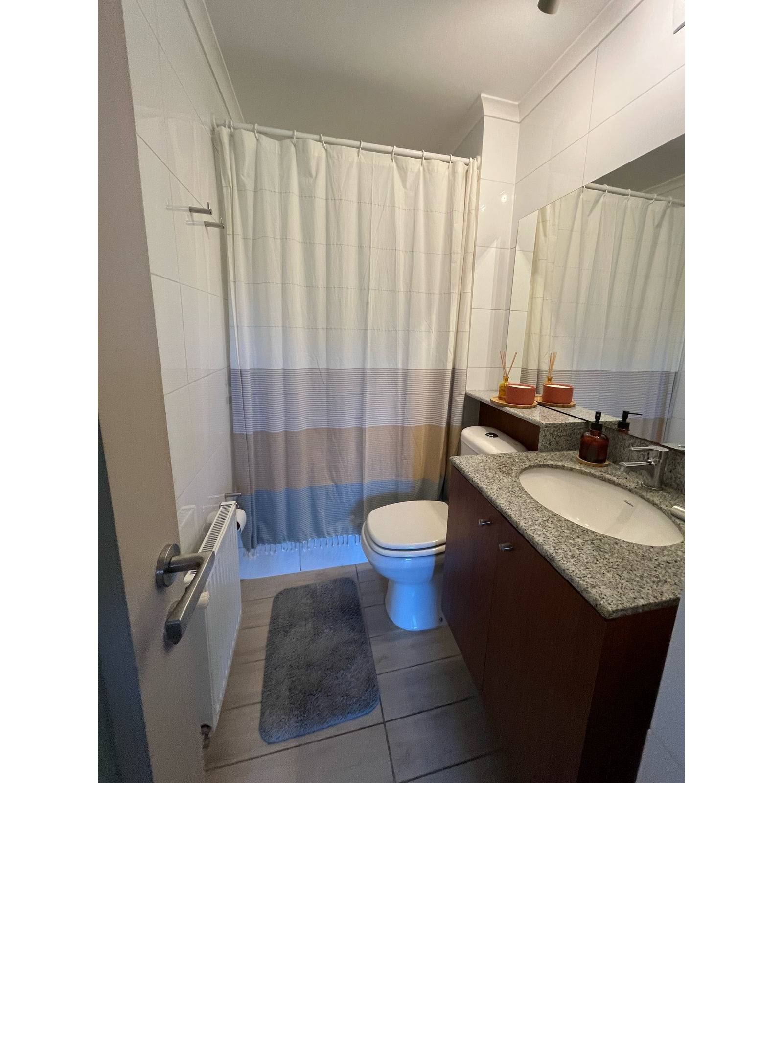 Baño con vanitorio de granito, espejo amplio y tina con cortina.