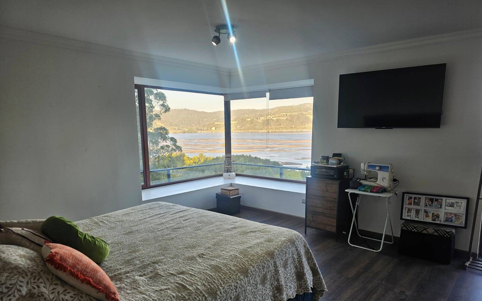 Dormitorio con cama matrimonial y ventanales en esquina.