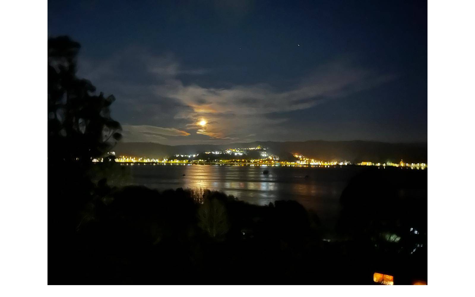 Vista nocturna de la bahía iluminada con luna llena.