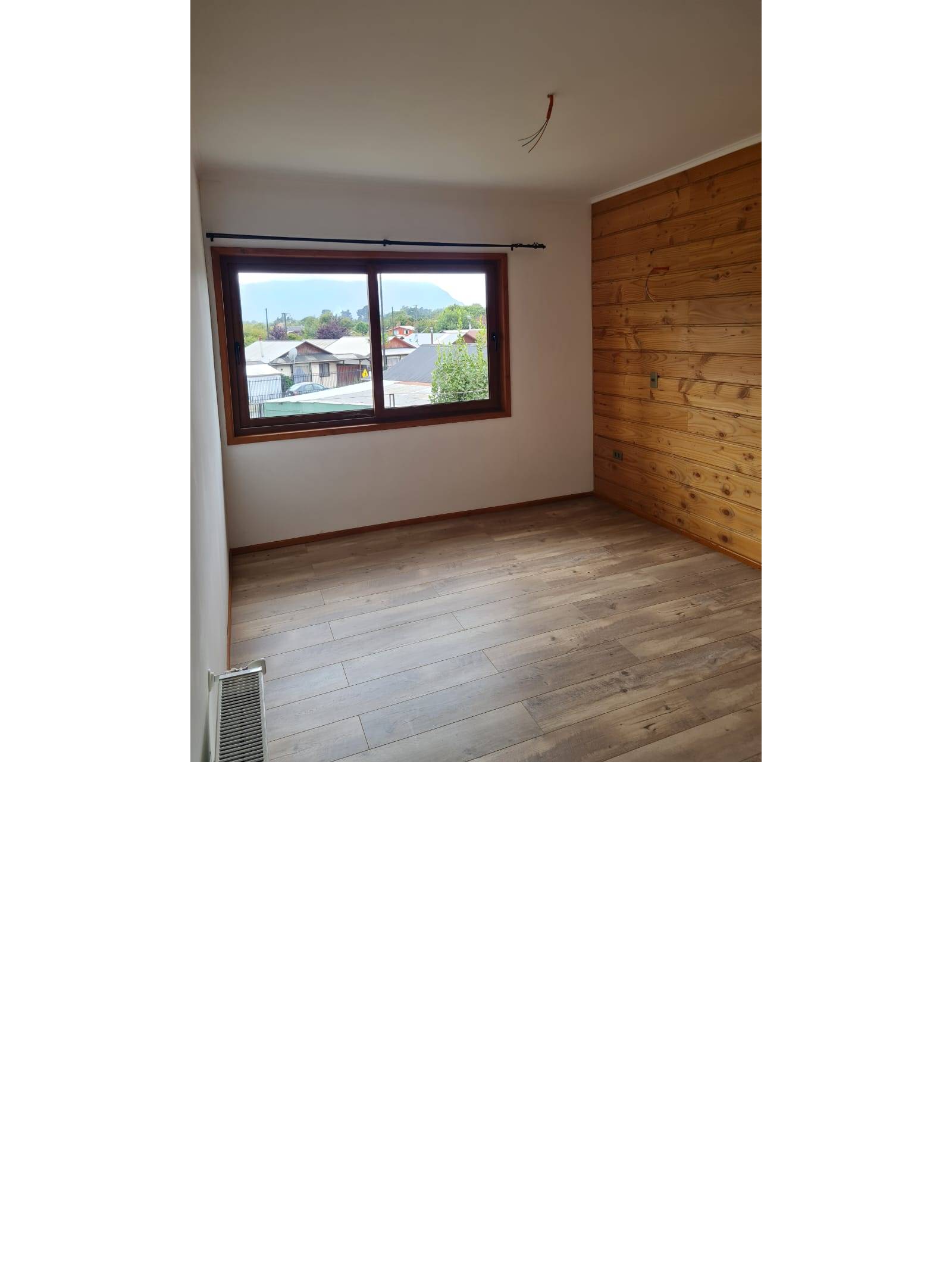 Dormitorio con pared revestida en madera y ventana amplia.