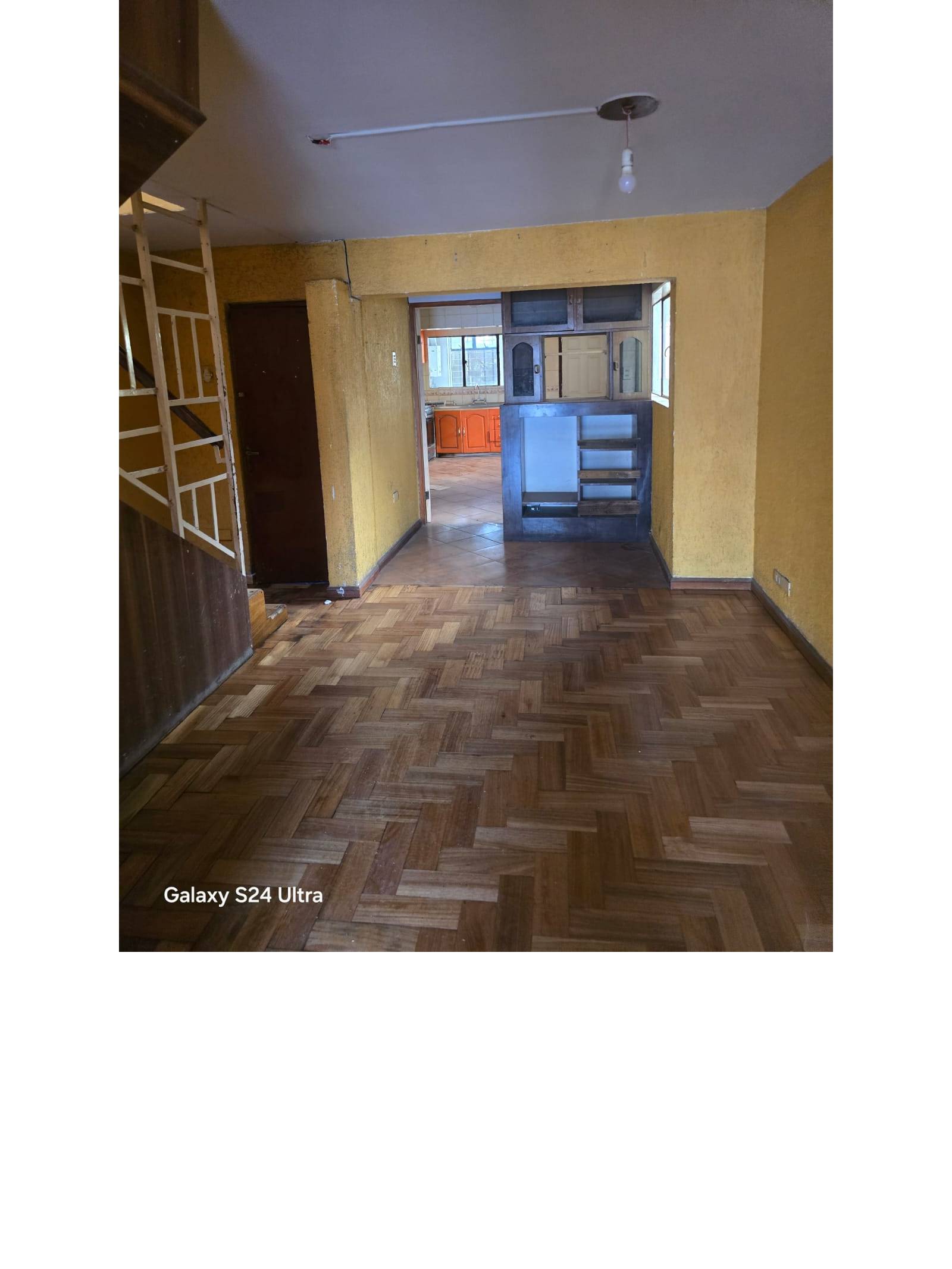 Estar con piso de parquet, escalera lateral y mueble divisor empotrado.