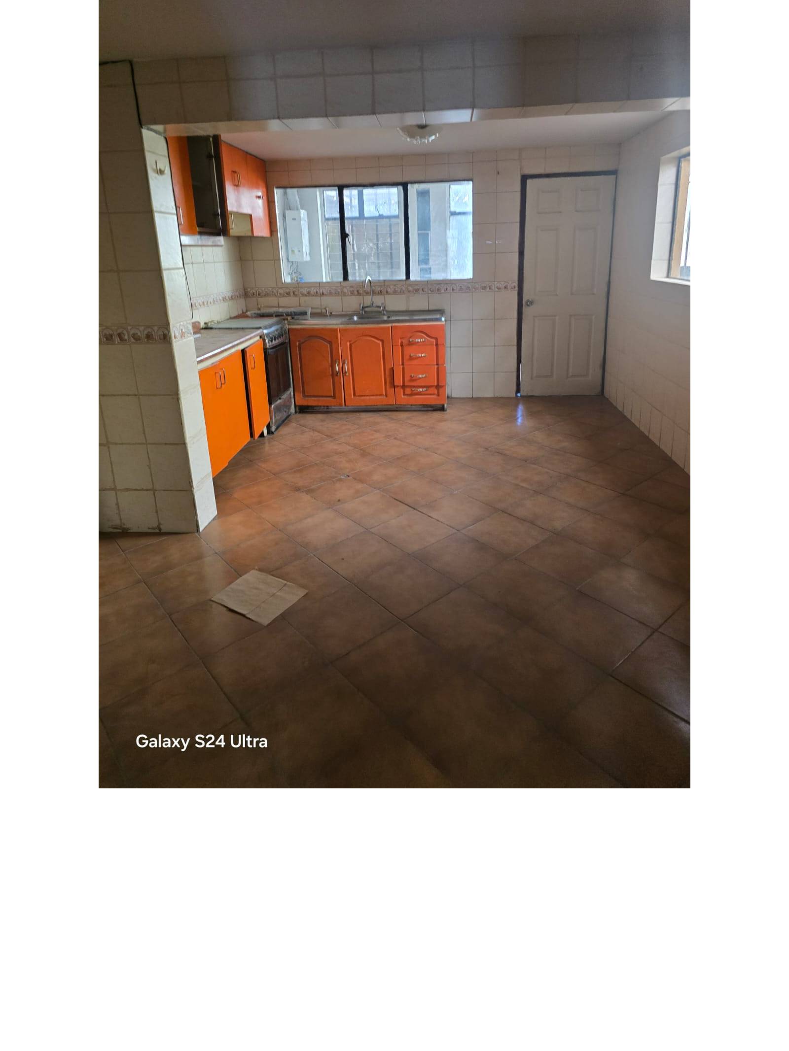 Cocina amplia con muebles naranjas, lavaplatos y ventana exterior.
