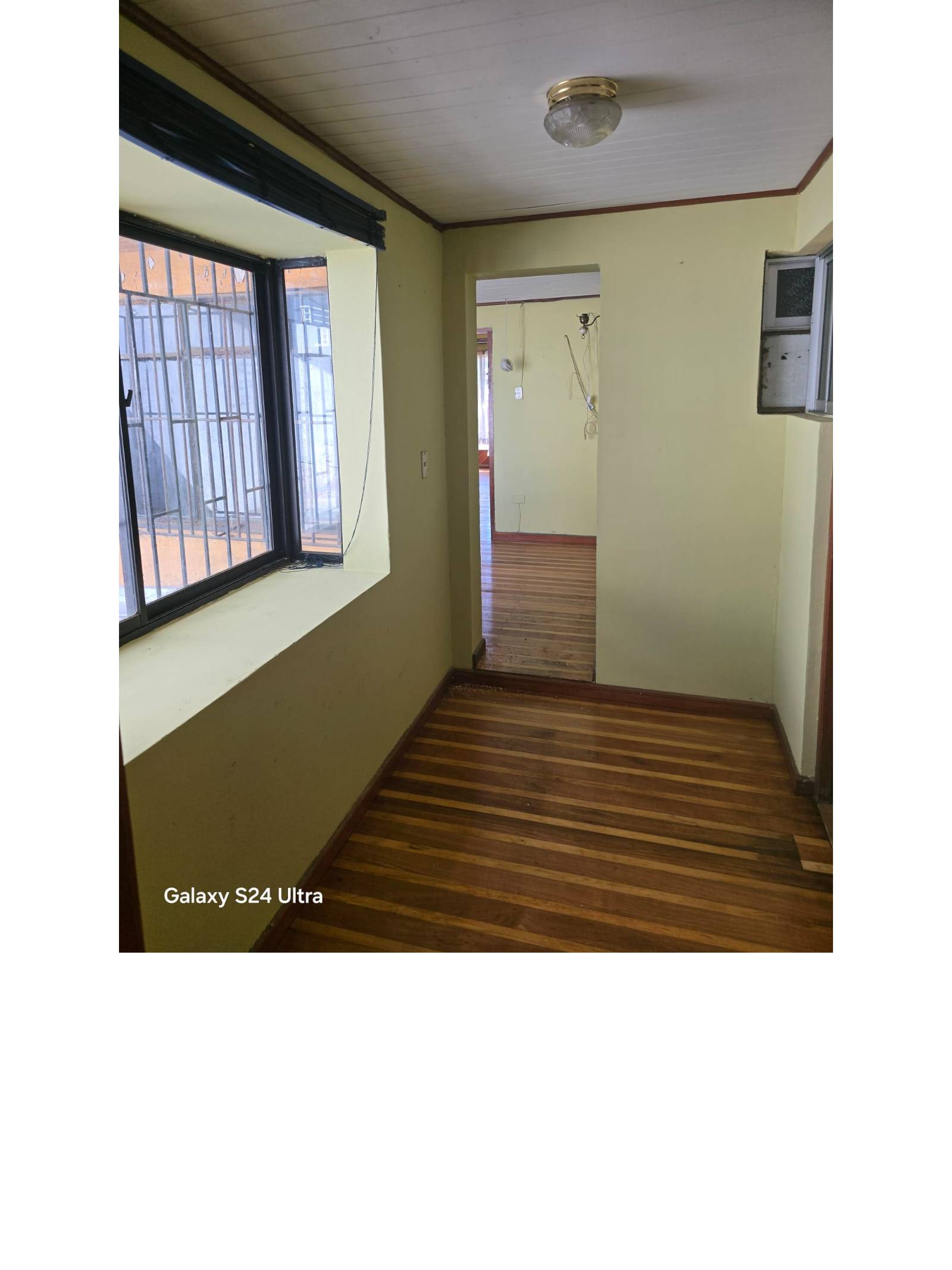 Pasillo interior con ventana enrejada y piso de madera.