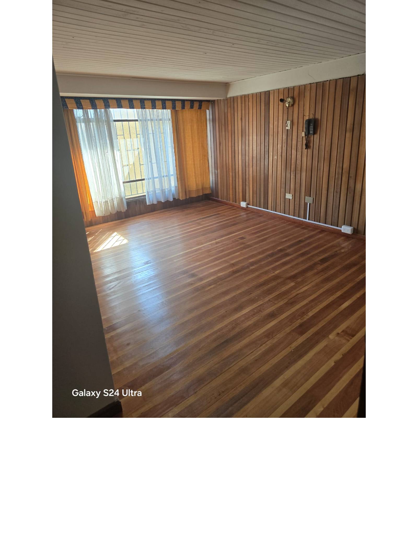 Dormitorio espacioso con pared revestida en madera y piso de madera.
