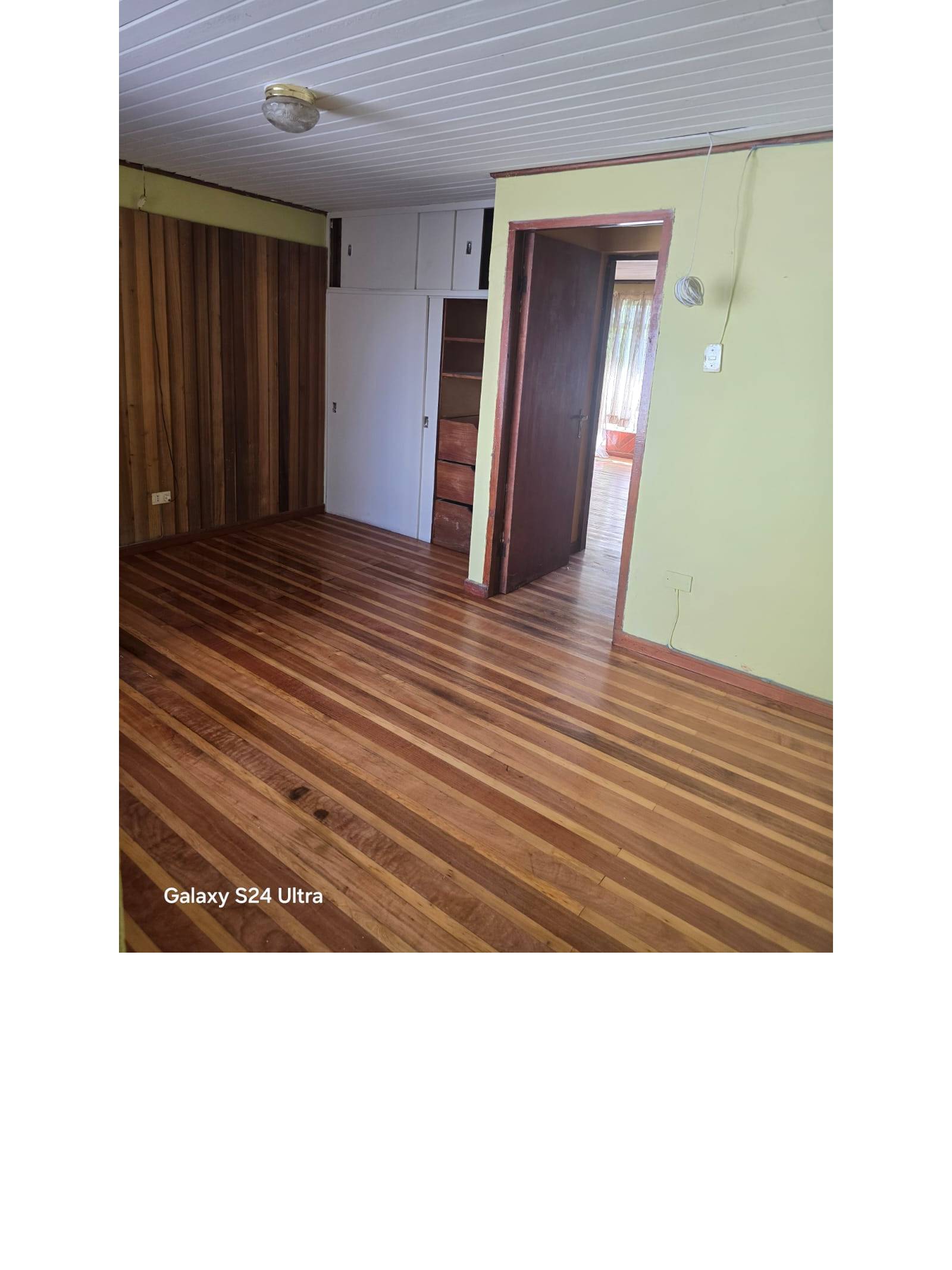 Habitación con clóset empotrado, pared de madera y acceso a otra pieza.