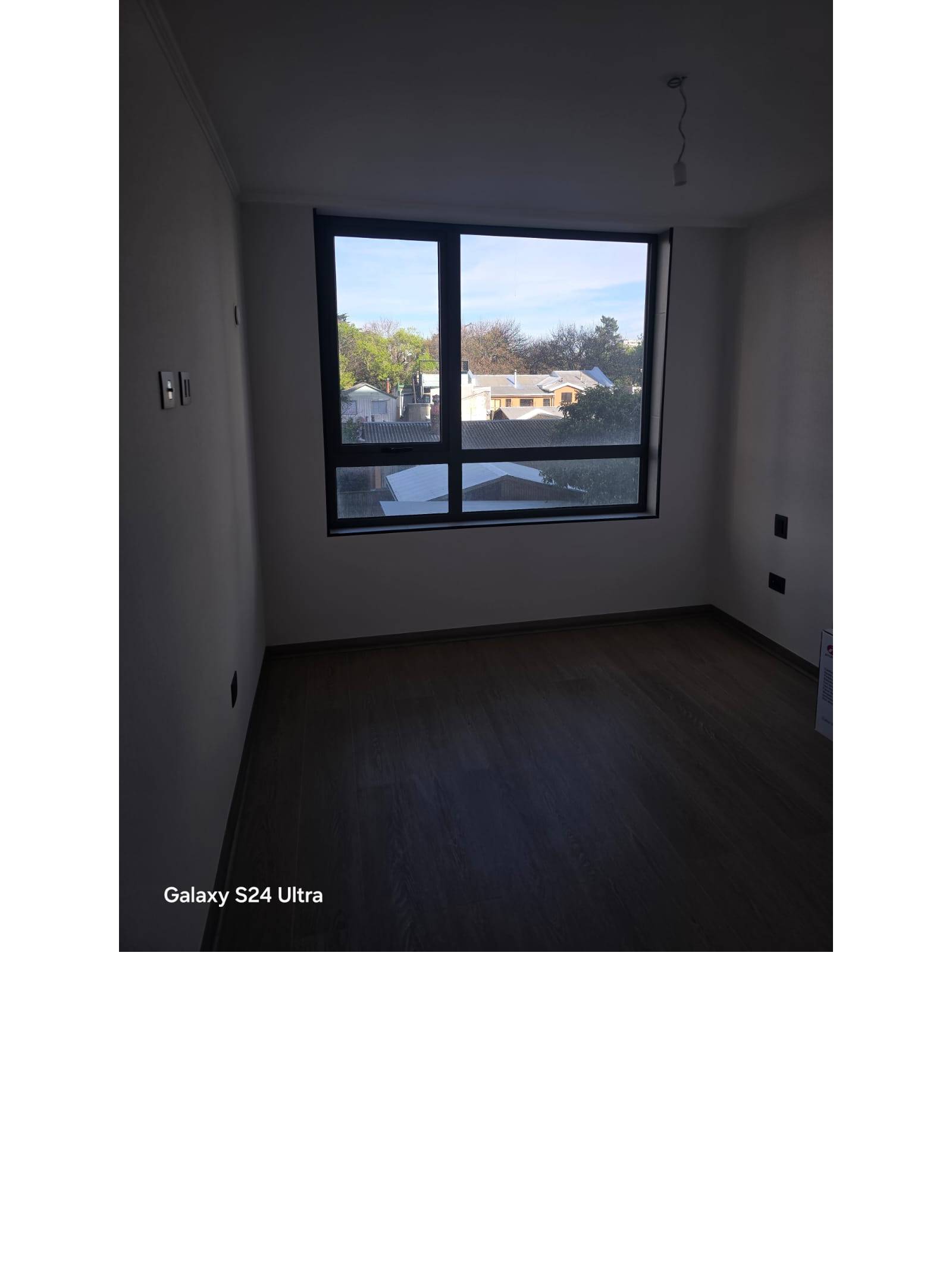 Dormitorio iluminado con amplio ventanal y piso fotolaminado.