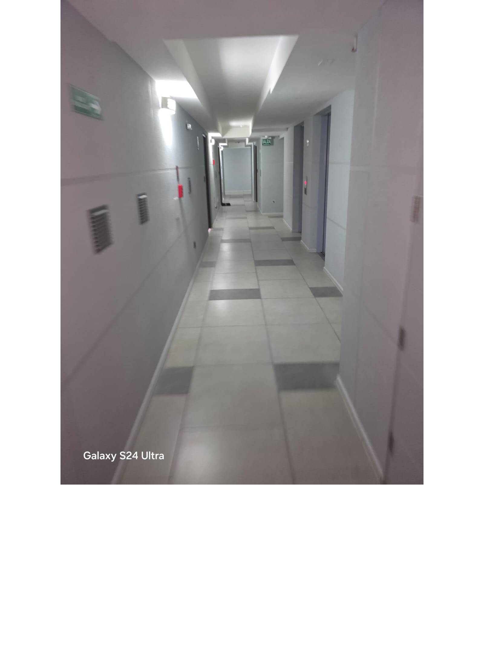 Pasillo común iluminado con puertas y ascensores del edificio.