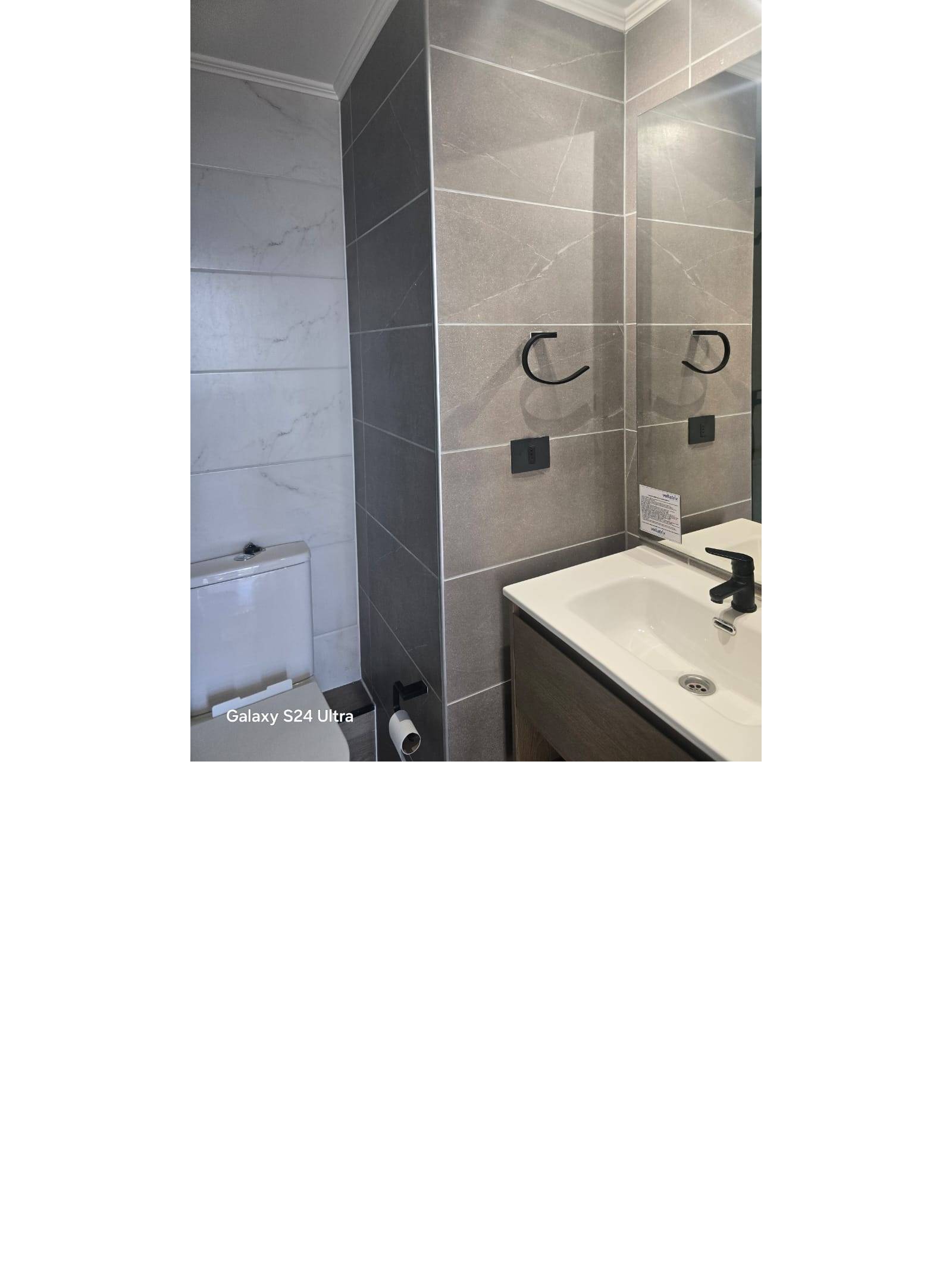 Baño moderno con vanitorio, espejo grande y muros revestidos en cerámica.