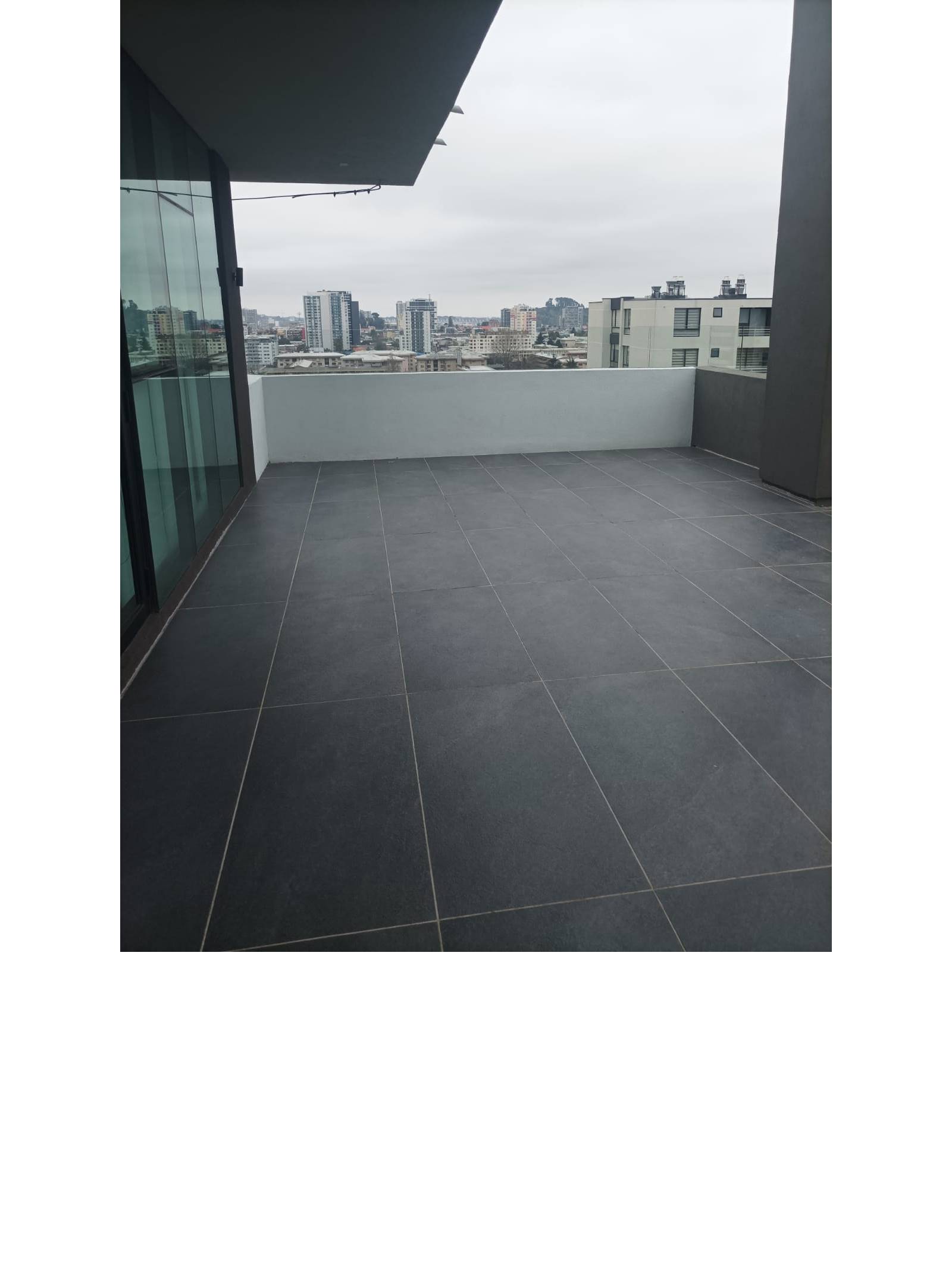 Terraza panorámica exterior con piso cerámico y baranda de cristal.