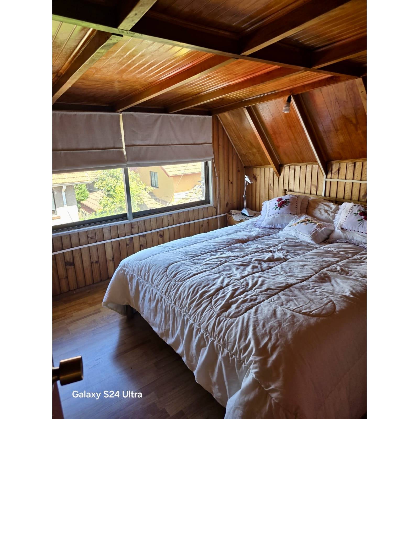 Dormitorio abuhardillado con revestimiento en madera y cama